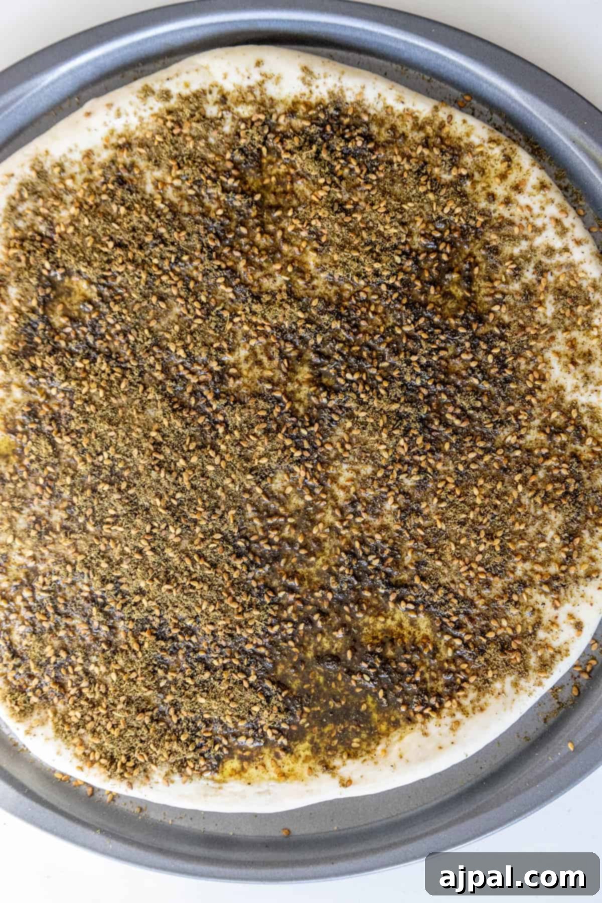 Aromatic Zaatar Pizza 7 A za'atar pizza is sitting on a pan with seeds on it.