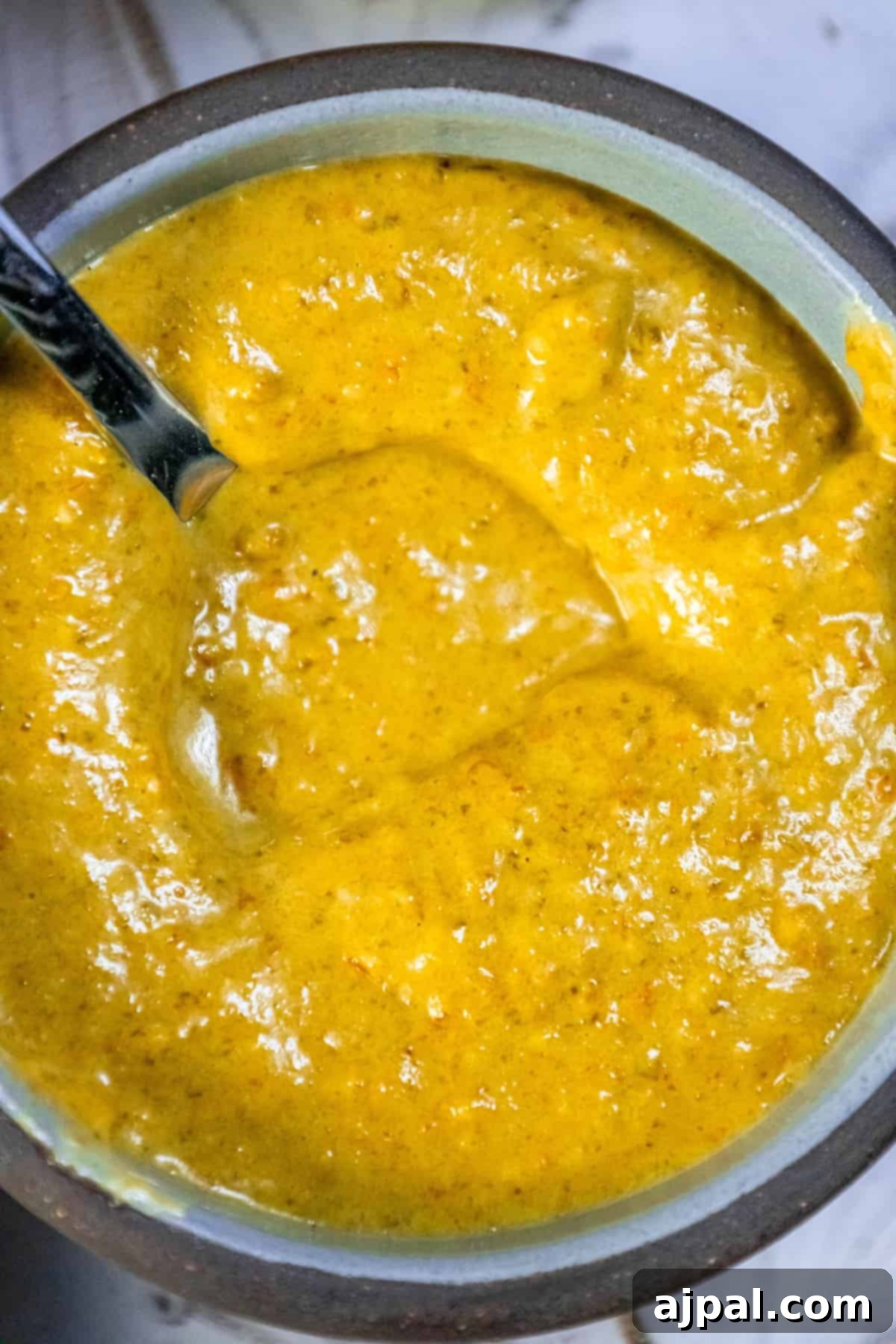 A bowl of vibrant yellow habanero sauce with a spoon resting in it, ready for tasting.