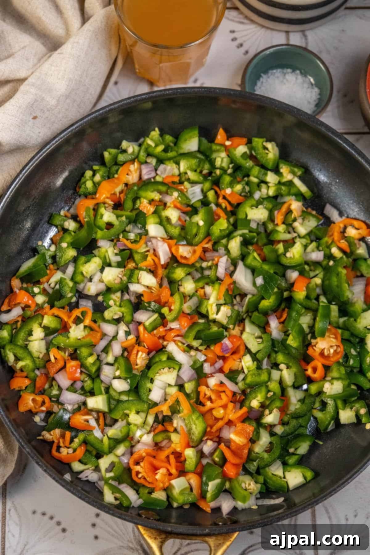 A frying pan with sautéing vegetables, including peppers, onion, and garlic, emitting aromatic steam.