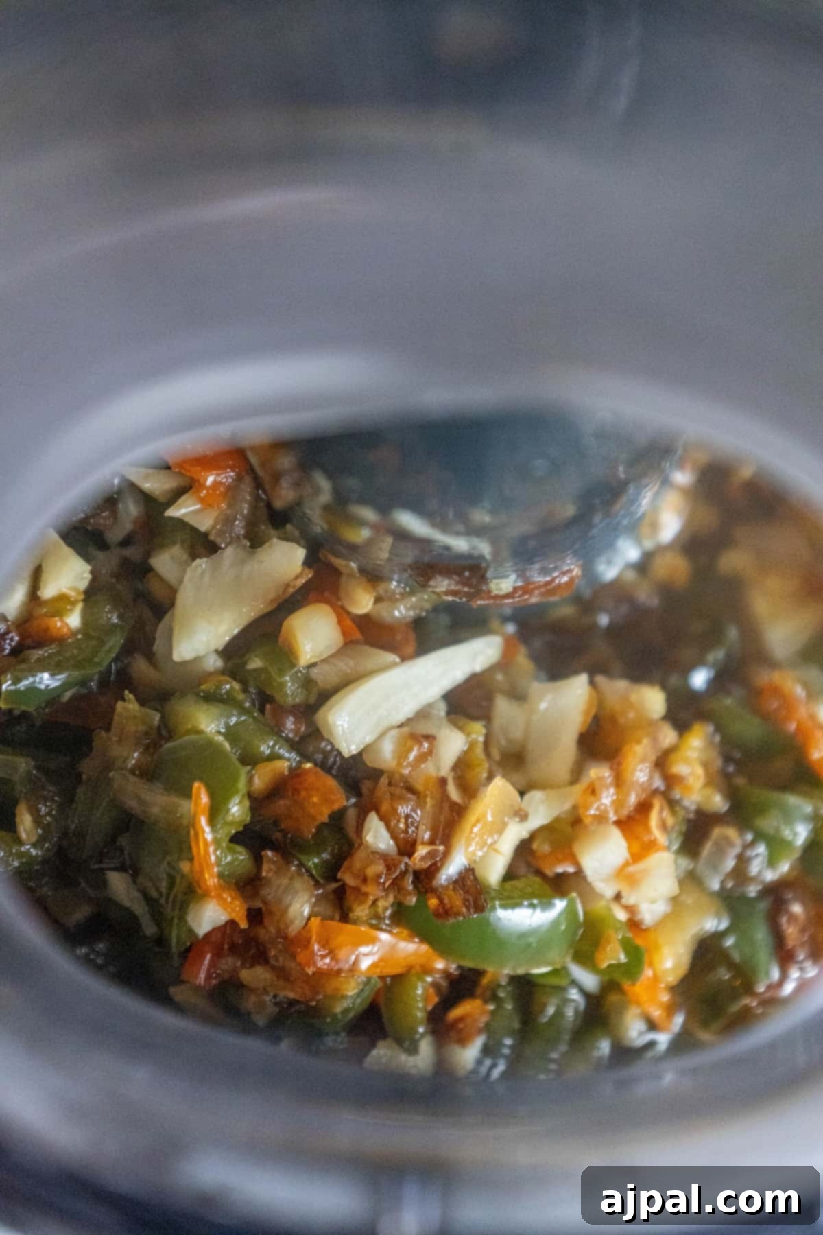 A food processor filled with blended vegetables, including peppers and other spices, forming a coarse hot sauce base.