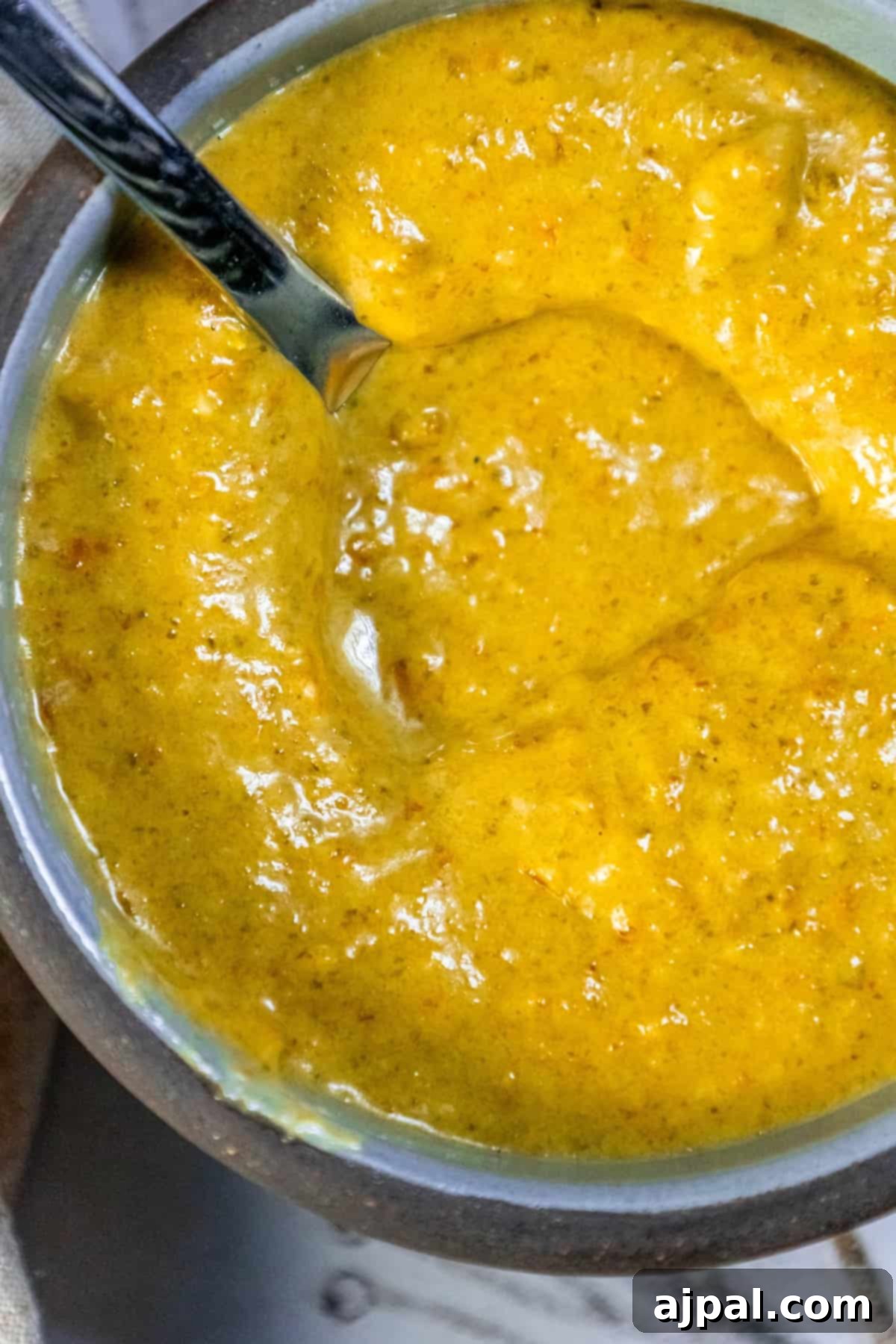 A bowl of comforting soup with a spoon, generously topped with a dash of homemade habanero hot sauce, adding a vibrant touch.