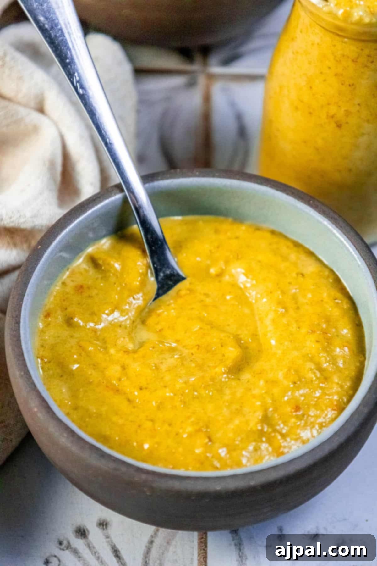 A bowl of rich, creamy soup with a spoon resting beside it, garnished with a subtle touch of homemade hot sauce.