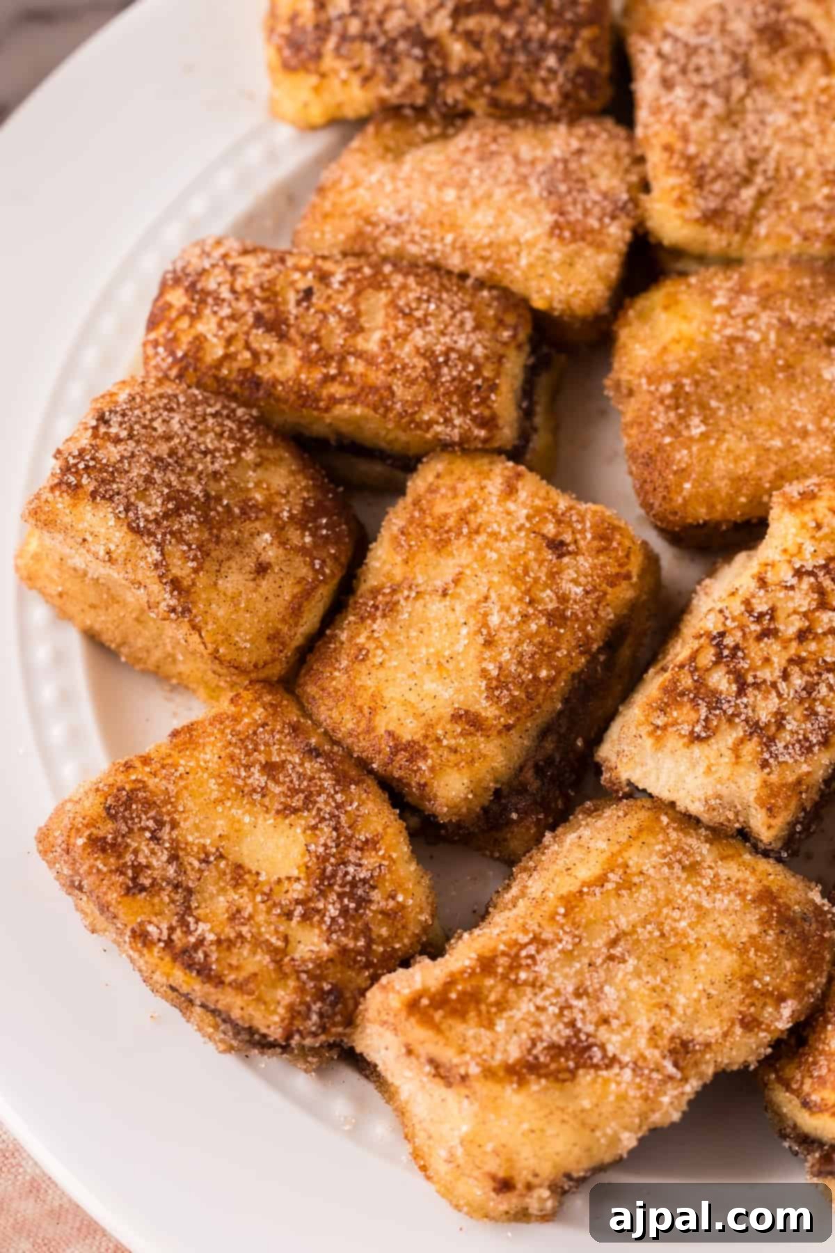 A plate of golden Nutella Stuffed French Toast bites with a light dusting of powdered sugar, presented on a marble surface.