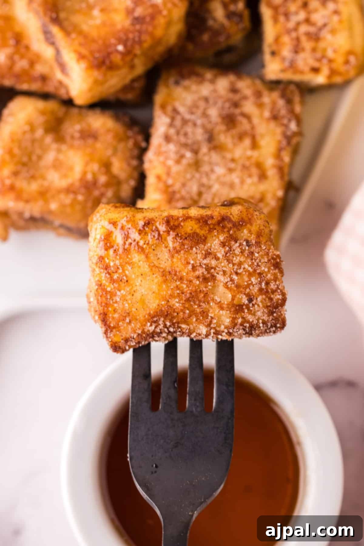 A French Toast bite stuffed with chocolate, held on a fork, showing the gooey Nutella filling.