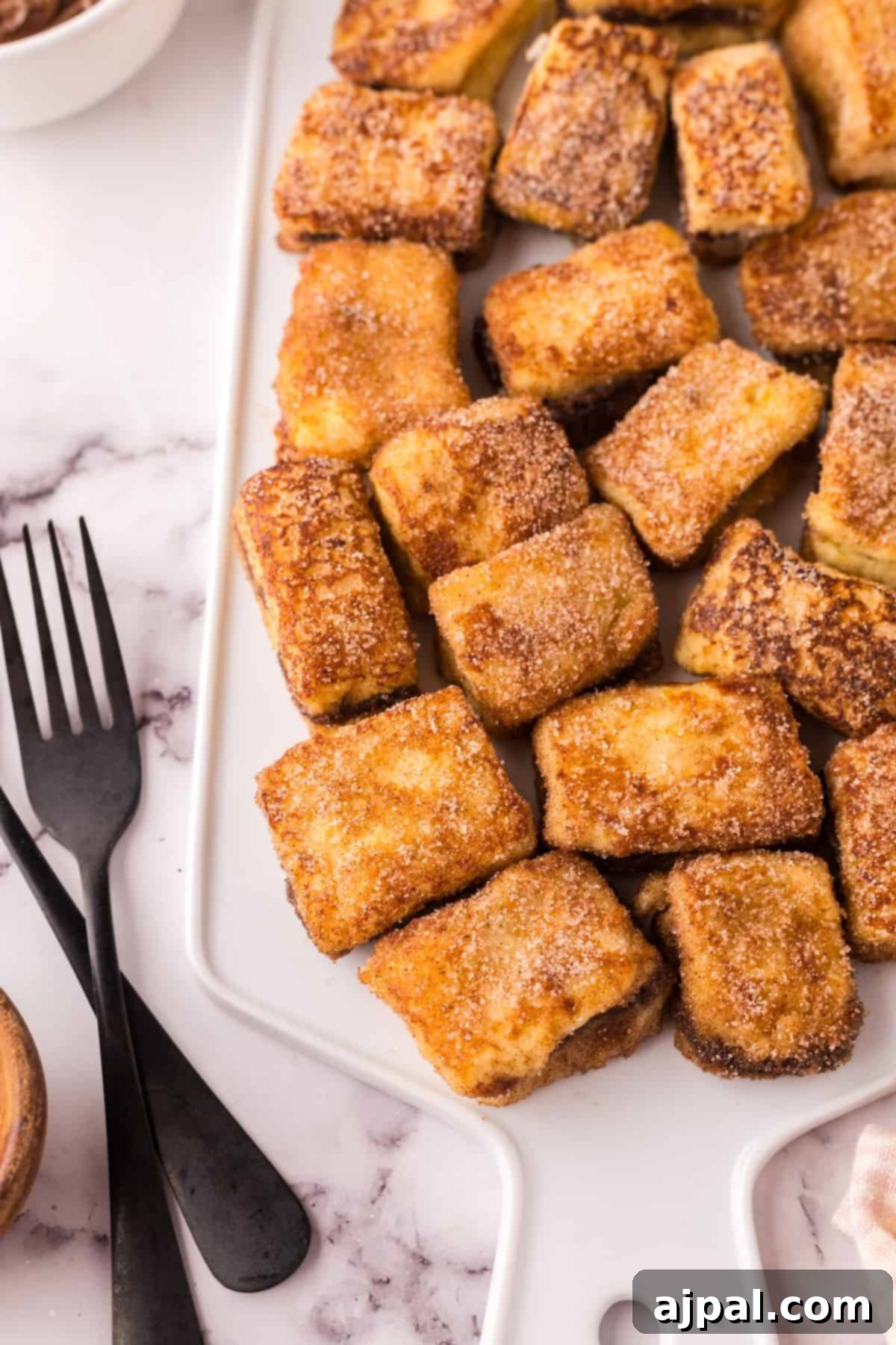 A beautiful plate of golden Nutella Stuffed French Toast bites, elegantly arranged on a marble surface.