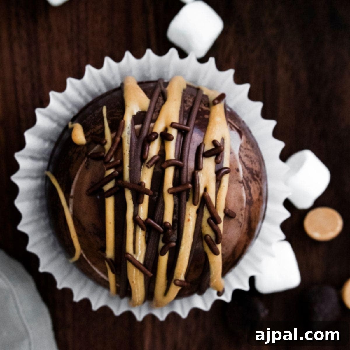 A peanut butter hot chocolate bomb-inspired chocolate cupcake with marshmallows and chocolate drizzle.