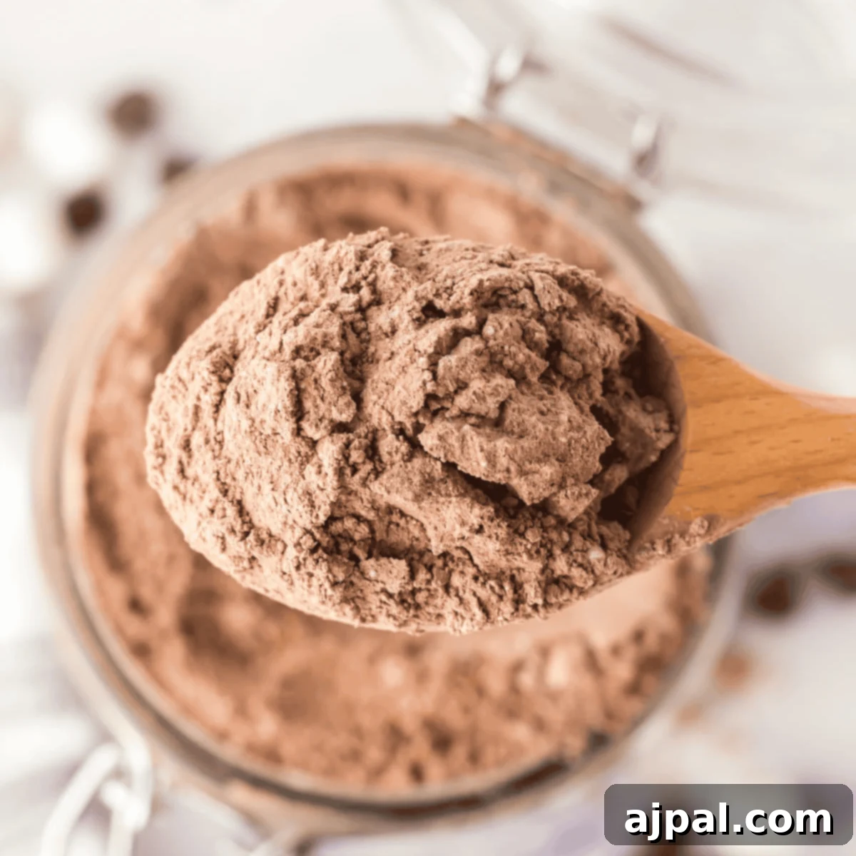 A wooden spoon scoops homemade hot cocoa mix from a jar, seen from above.
