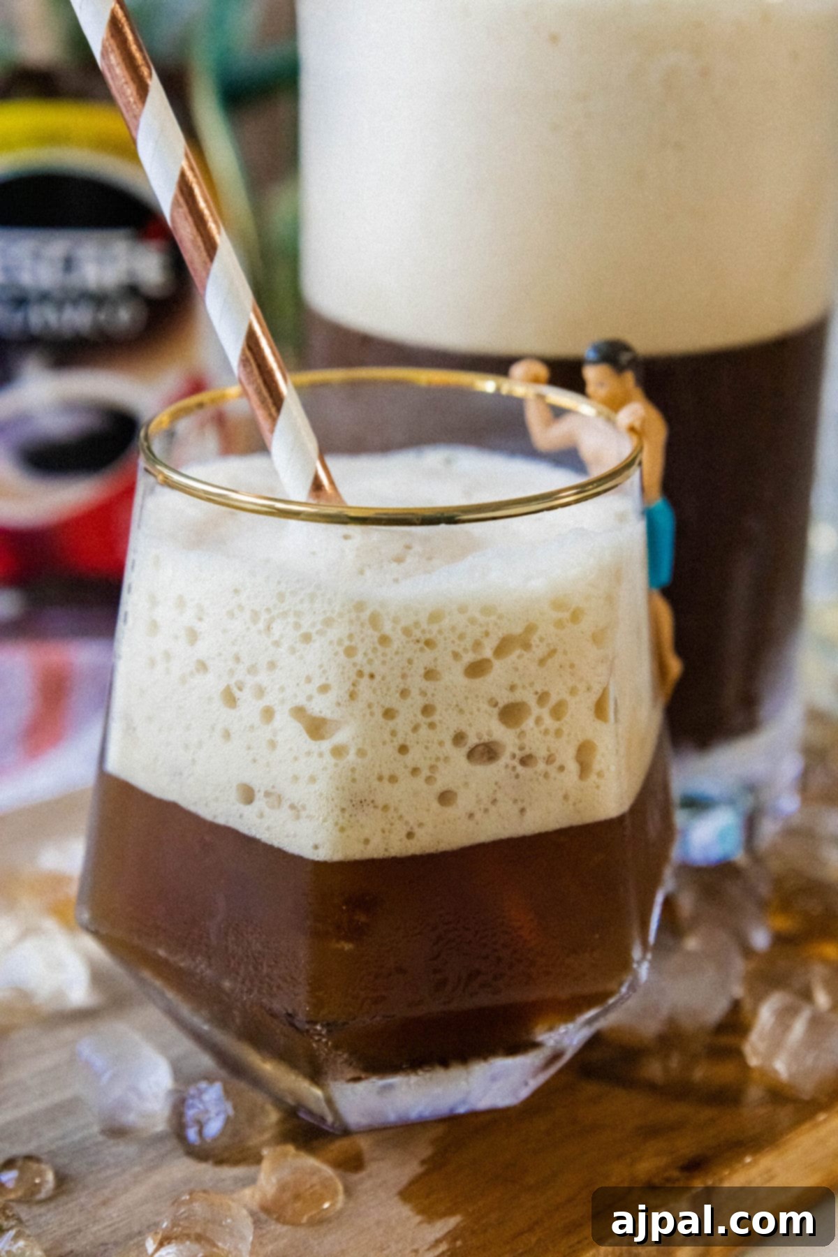 whipped Greek frappé coffee in a glass with ice and foam and a paper straw on a table
