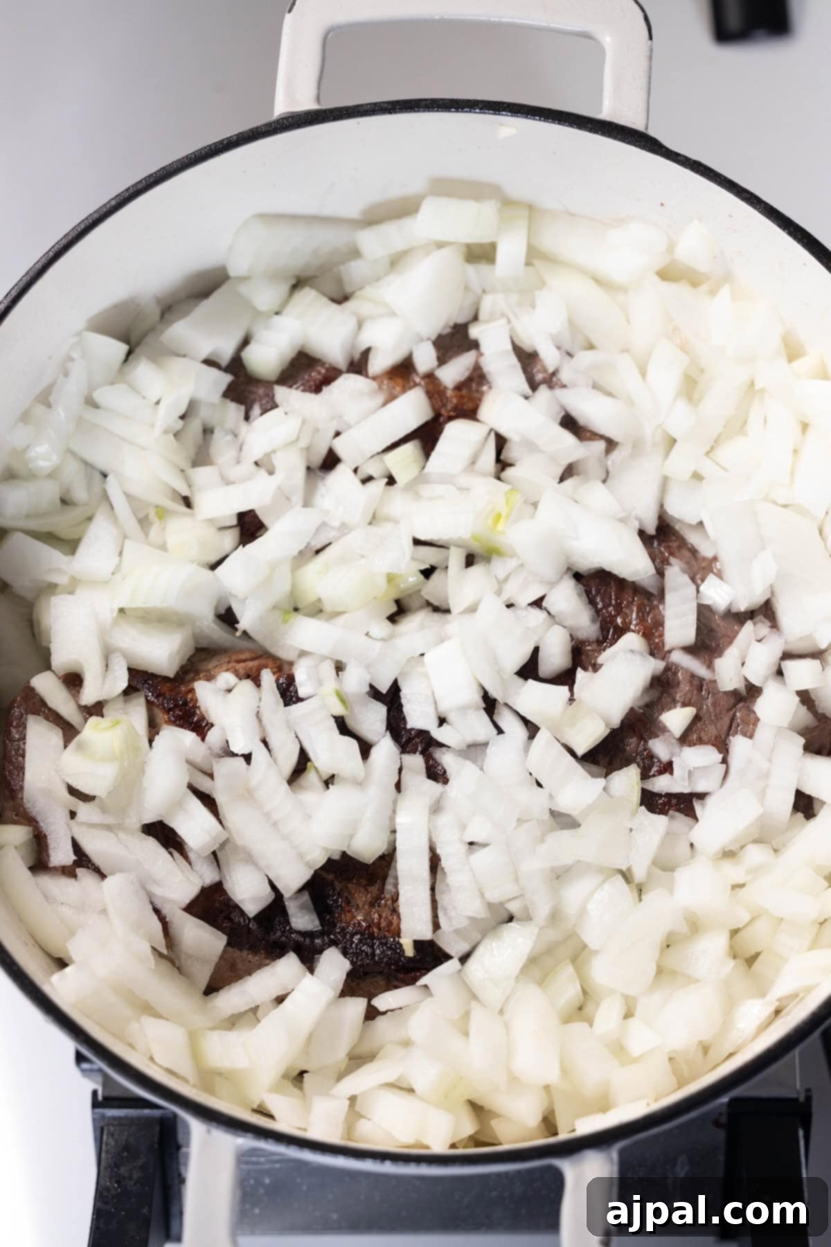 Adding chopped onions to browned meat in a pot.