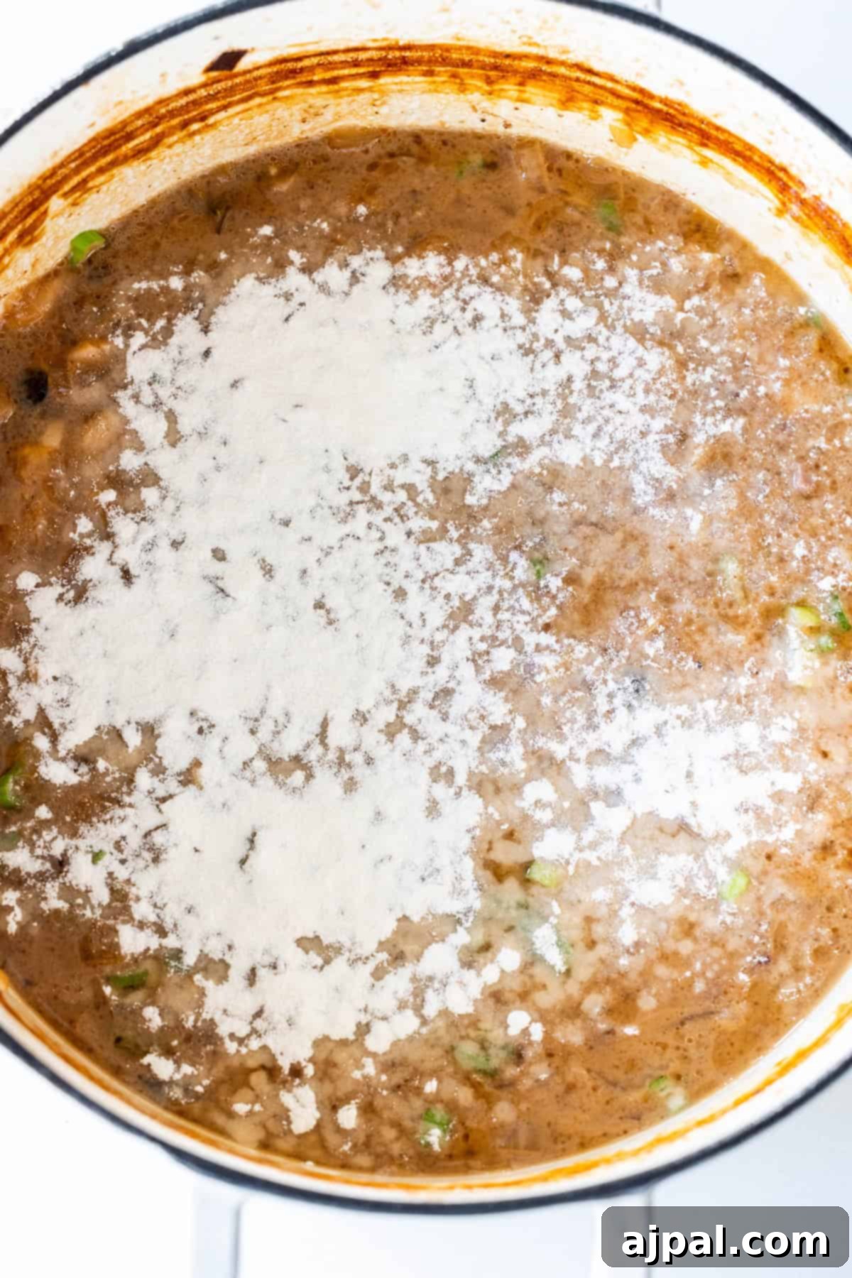 Flour being sprinkled over onion soup to thicken it.