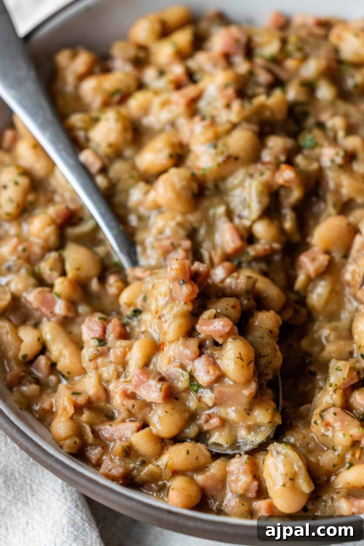 A bowl of brothy ham and beans with diced ham and herbs