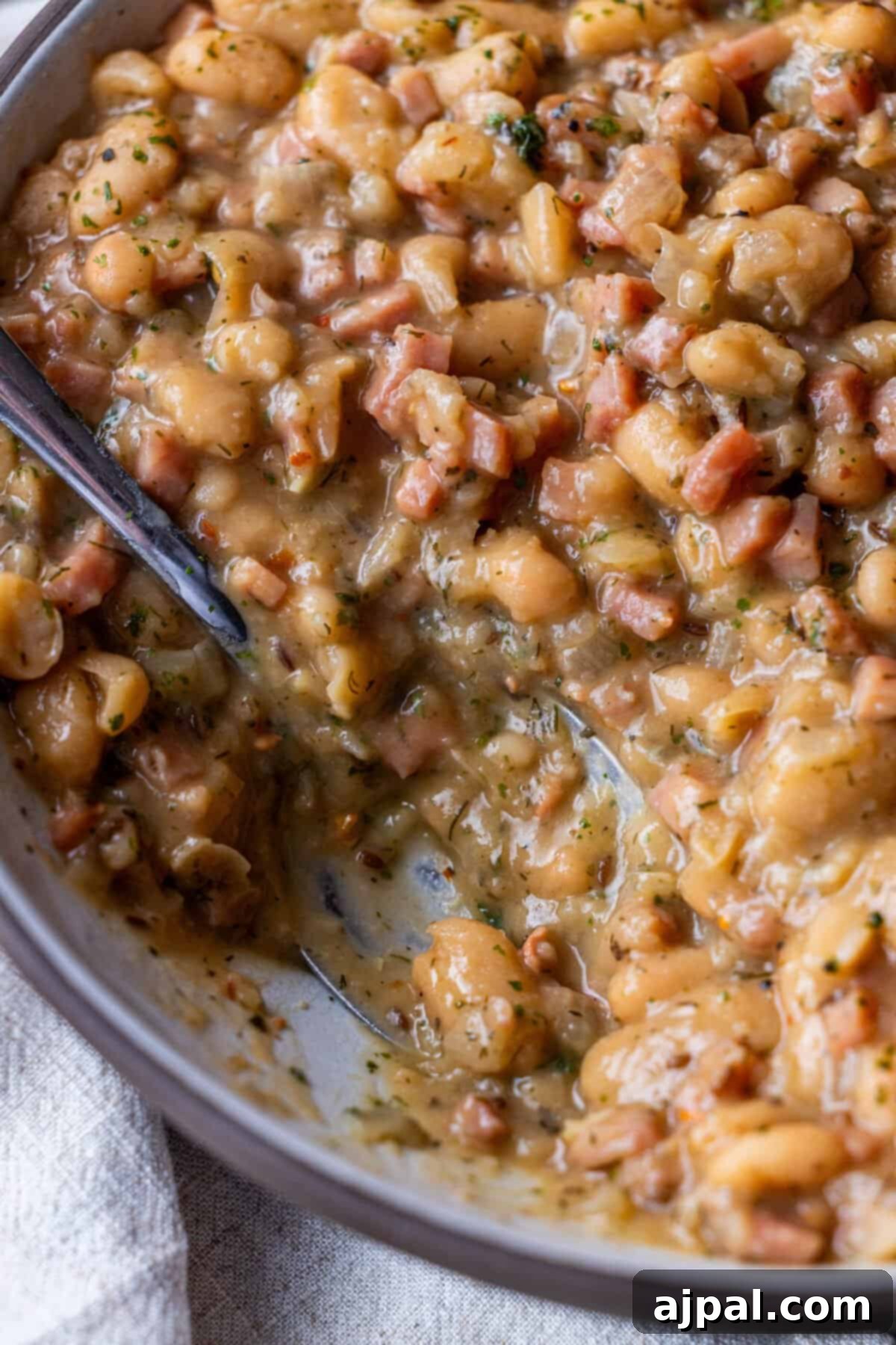 Close-up of creamy bean stew with chunks of ham and herbs