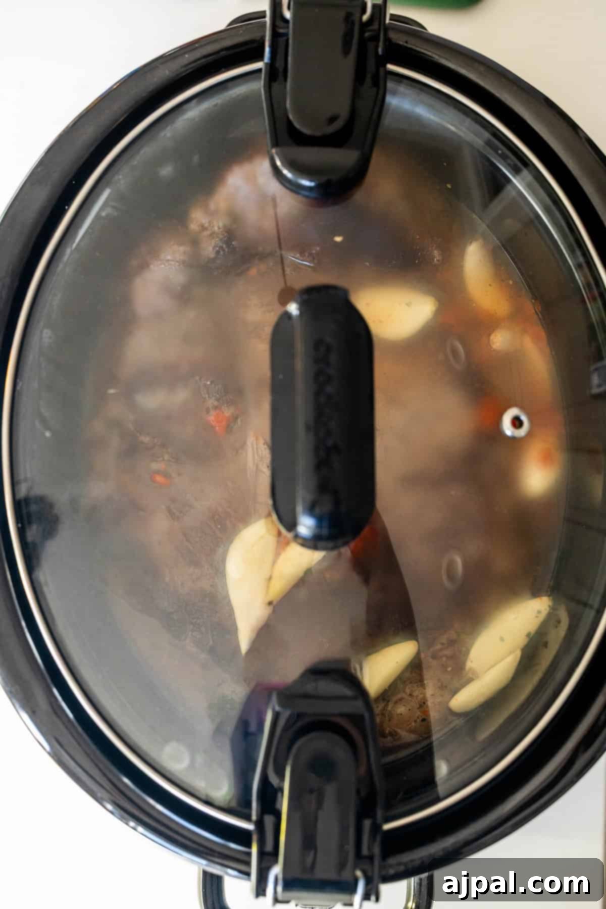 Slow cooker with a chuck roast, garlic cloves, and broth