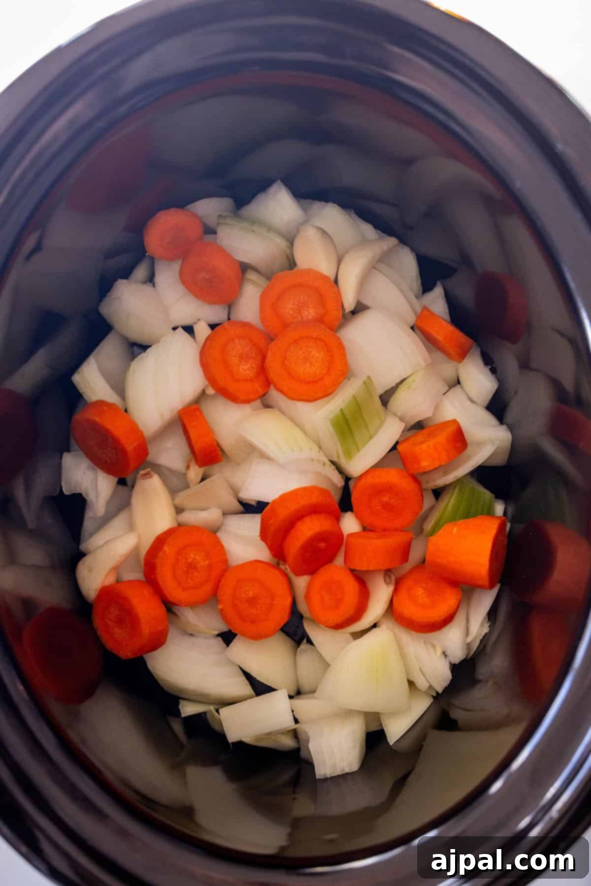 Chopped vegetables at the bottom of a slow cooker