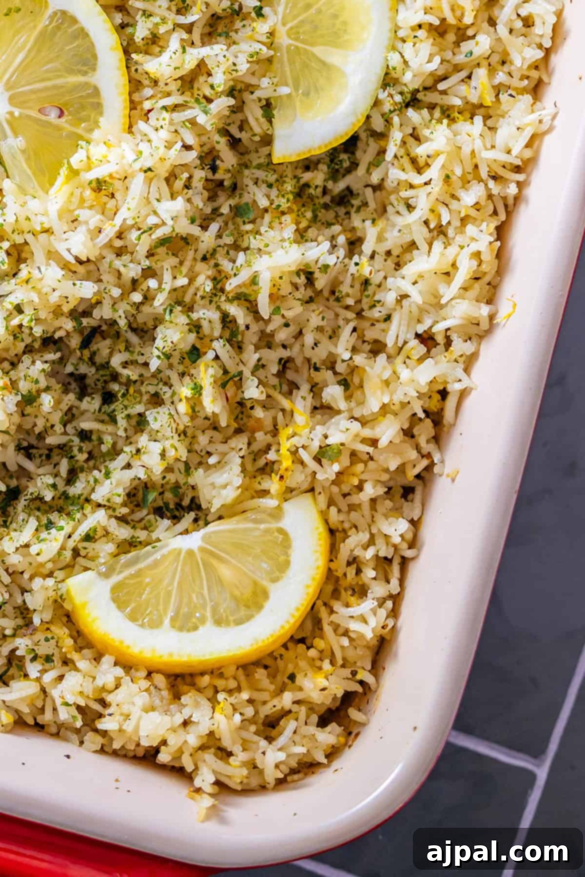Close-up of baked lemon rice with herbs and lemon wedges.