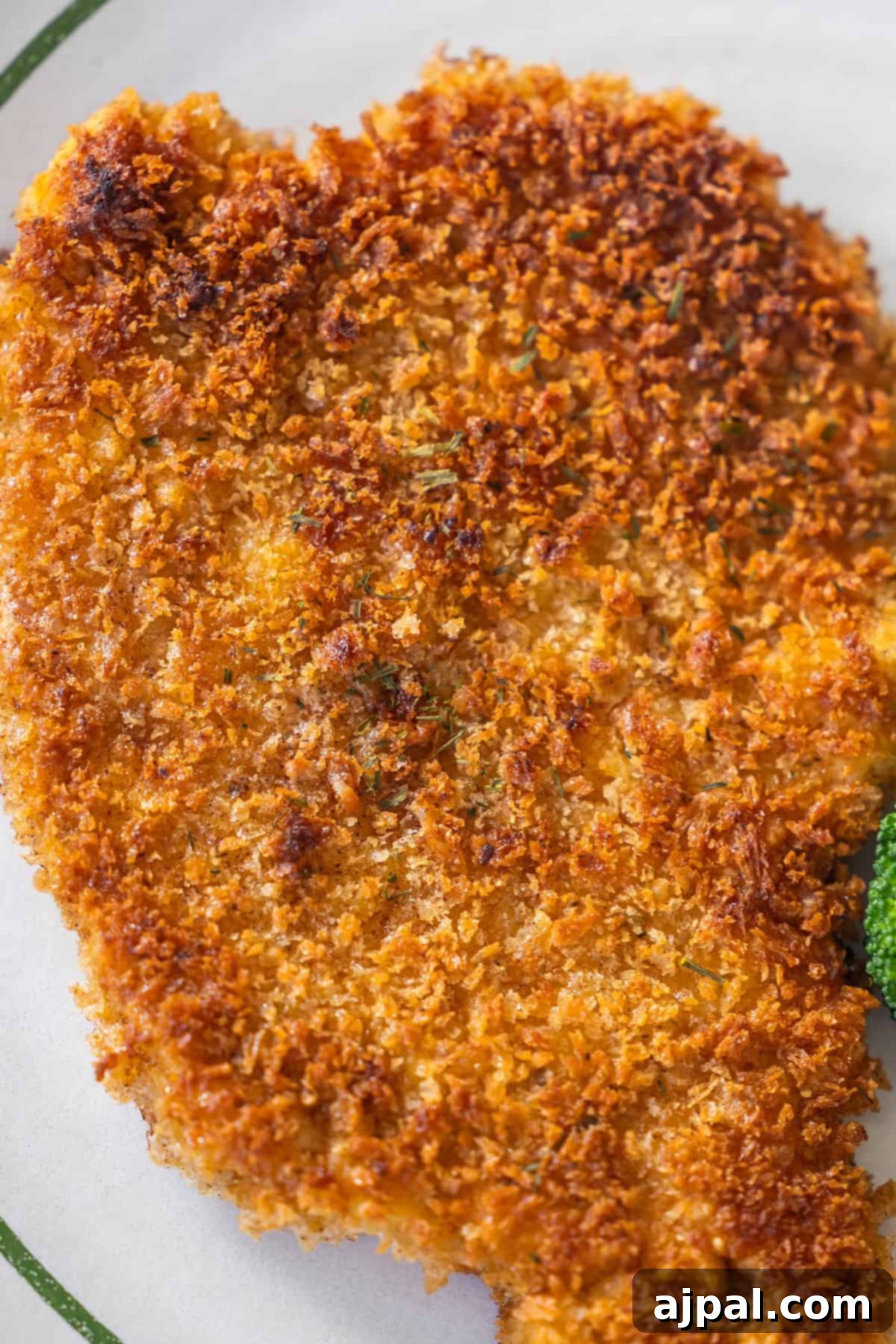 Pork Schnitzel: A Crispy, Golden Delight 2 Close-up of a golden-brown breaded Pork Schnitzel on a white plate, showing its crispy texture and part of a green garnish.