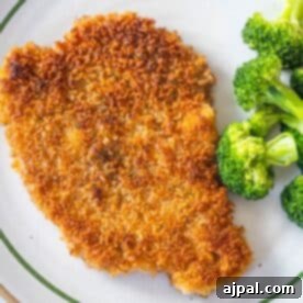 Pork Schnitzel: A Crispy, Golden Delight 13 A golden-brown chicken cutlet, inspired by a classic Schnitzel recipe, is served alongside steamed broccoli on a white plate with a green rim.
