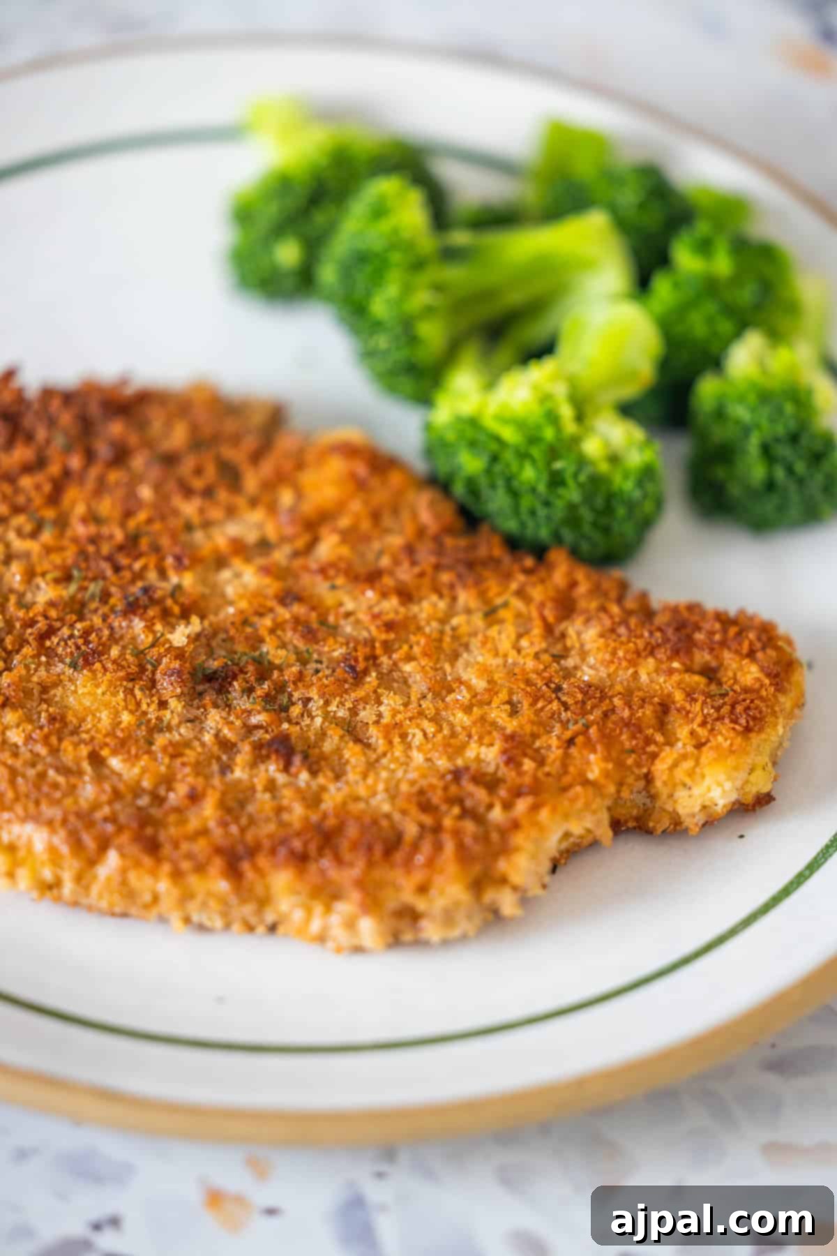 Pork Schnitzel: A Crispy, Golden Delight 3 A breaded and fried pork schnitzel is served on a white plate with a side of steamed broccoli—a classic pork recipe for any schnitzel lover.