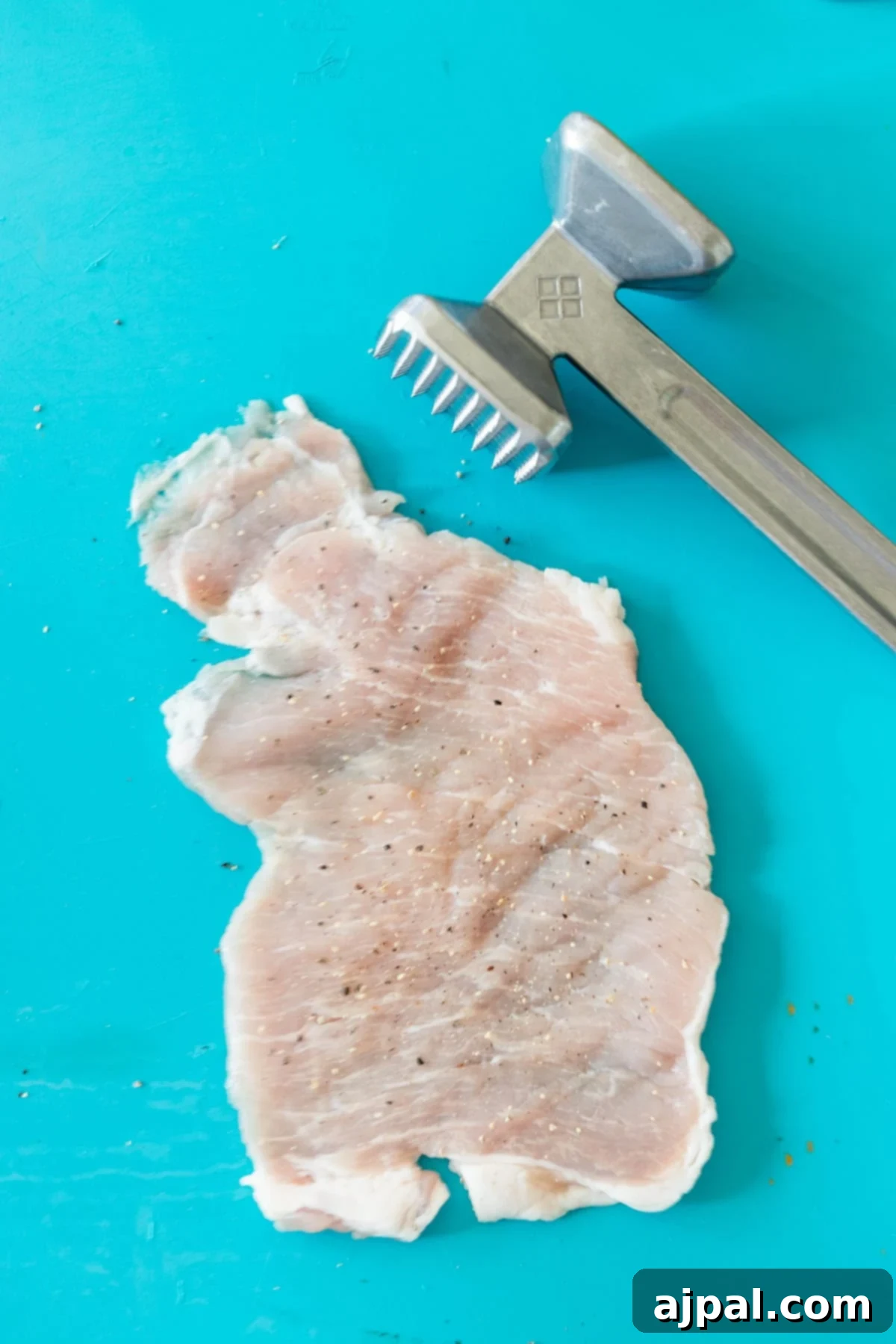 A raw chicken breast has been flattened with a meat tenderizer, ready for your favorite schnitzel recipe, both resting on a bright turquoise surface.