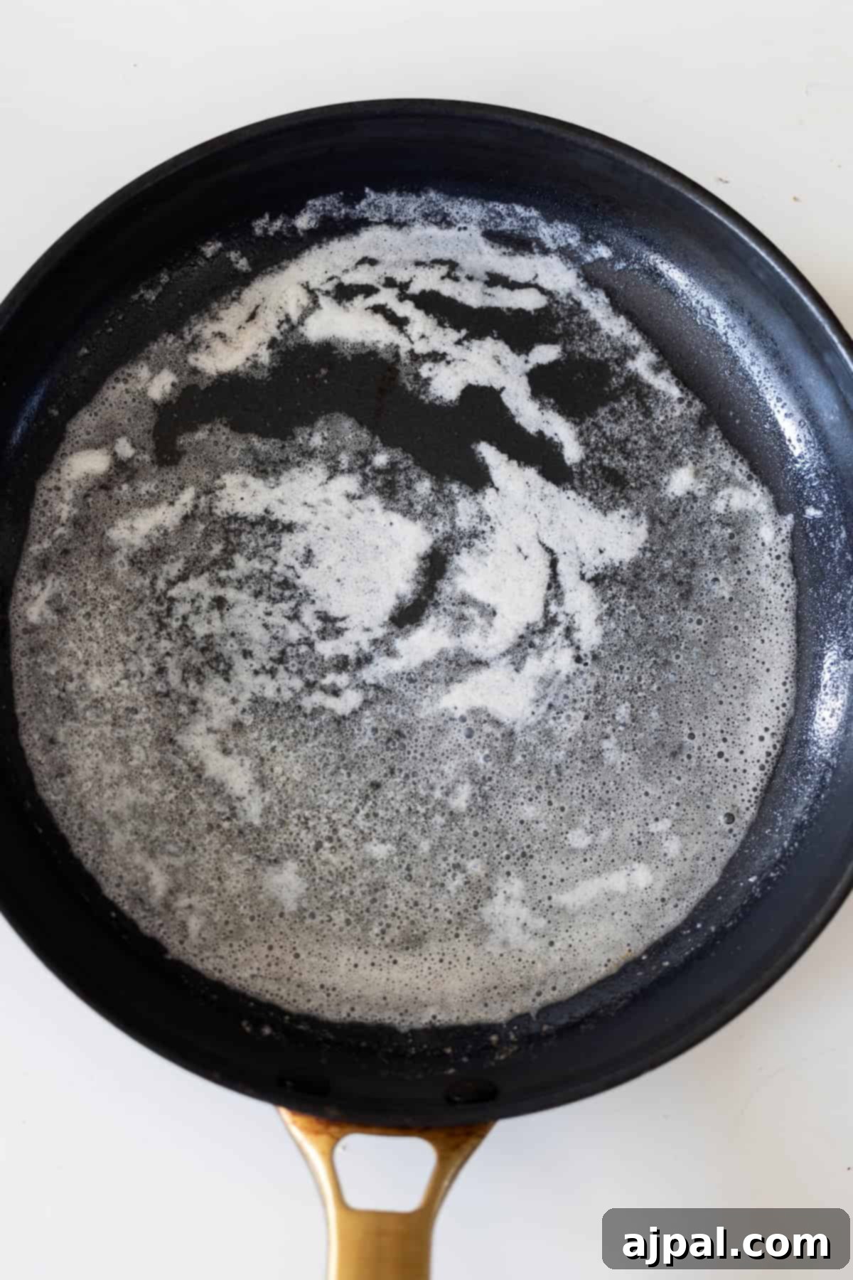 A black skillet with melted butter, forming white, frothy bubbles and streaks, sits on a white surface—perfect for starting a classic Pork Schnitzel recipe.