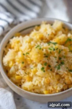 A bowl of Corn Rice, mixed with corn and garnished with chopped herbs, sits on a table with a striped cloth in the background.