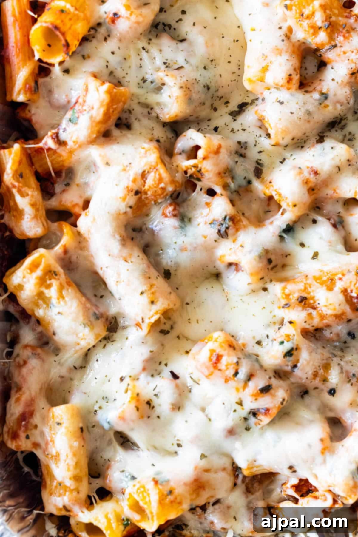 Close-up of cheesy baked rigatoni topped with melted cheese and sprinkled herbs.