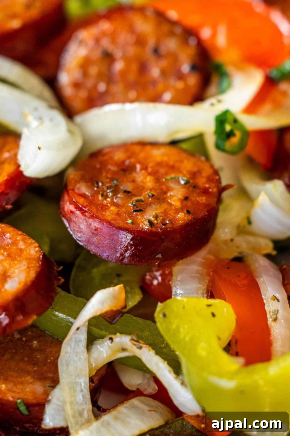 Close-up of sliced sausage, onions, green and red bell peppers cooked together and seasoned with herbs—a flavorful Sheetpan Kielbasa and Peppers dinner.