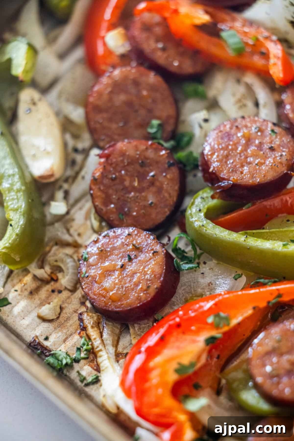 Kielbasa, red and green peppers, and onions roasted on a sheetpan, then garnished with chopped herbs.