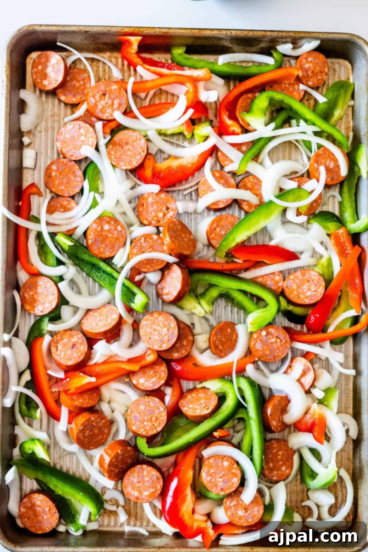 A baking sheet topped with sliced pepperoni, green and red bell peppers, onion slices, and hearty kielbasa makes for an easy Sheetpan Dinner—all spread out and ready for cooking.