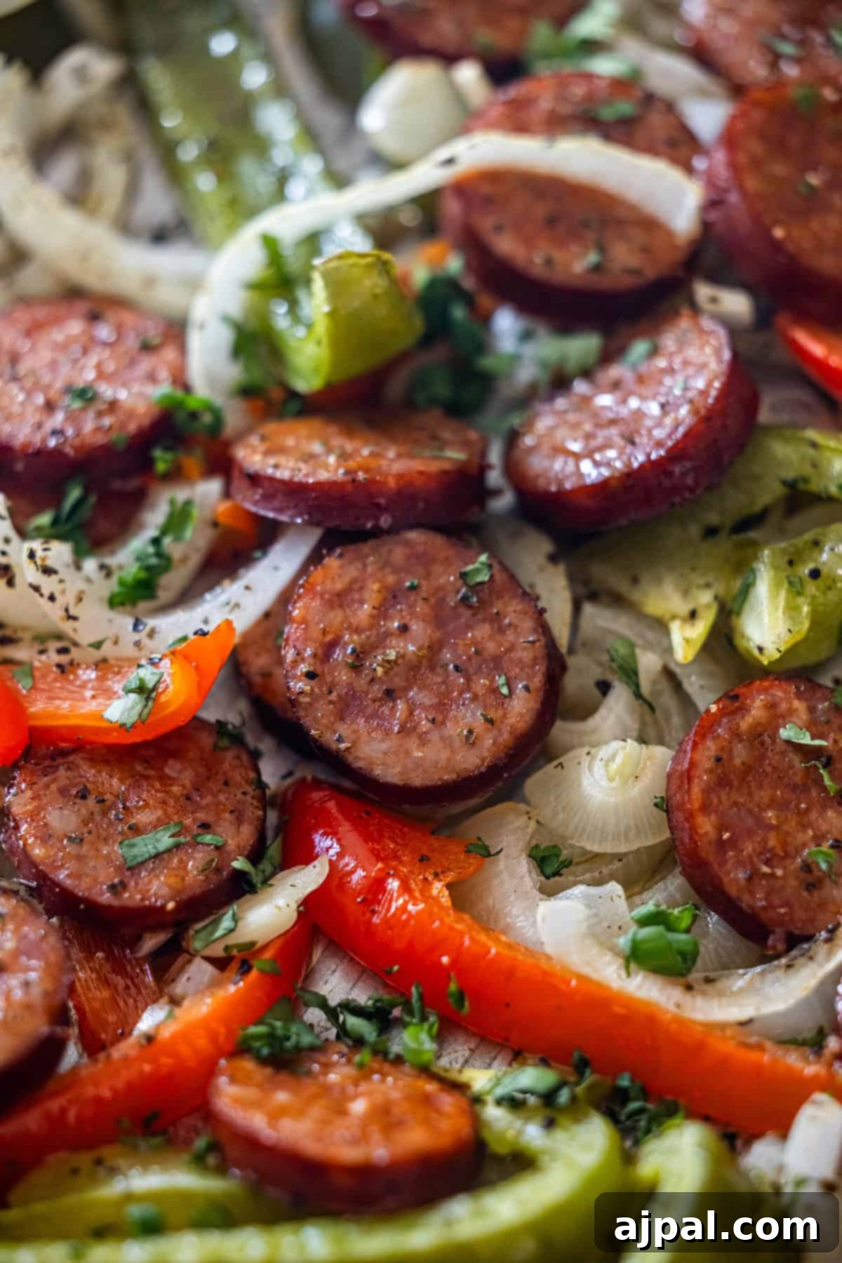 Sliced sausage, onions, and colorful peppers seasoned with herbs, arranged for a flavorful Sheetpan Kielbasa dinner.