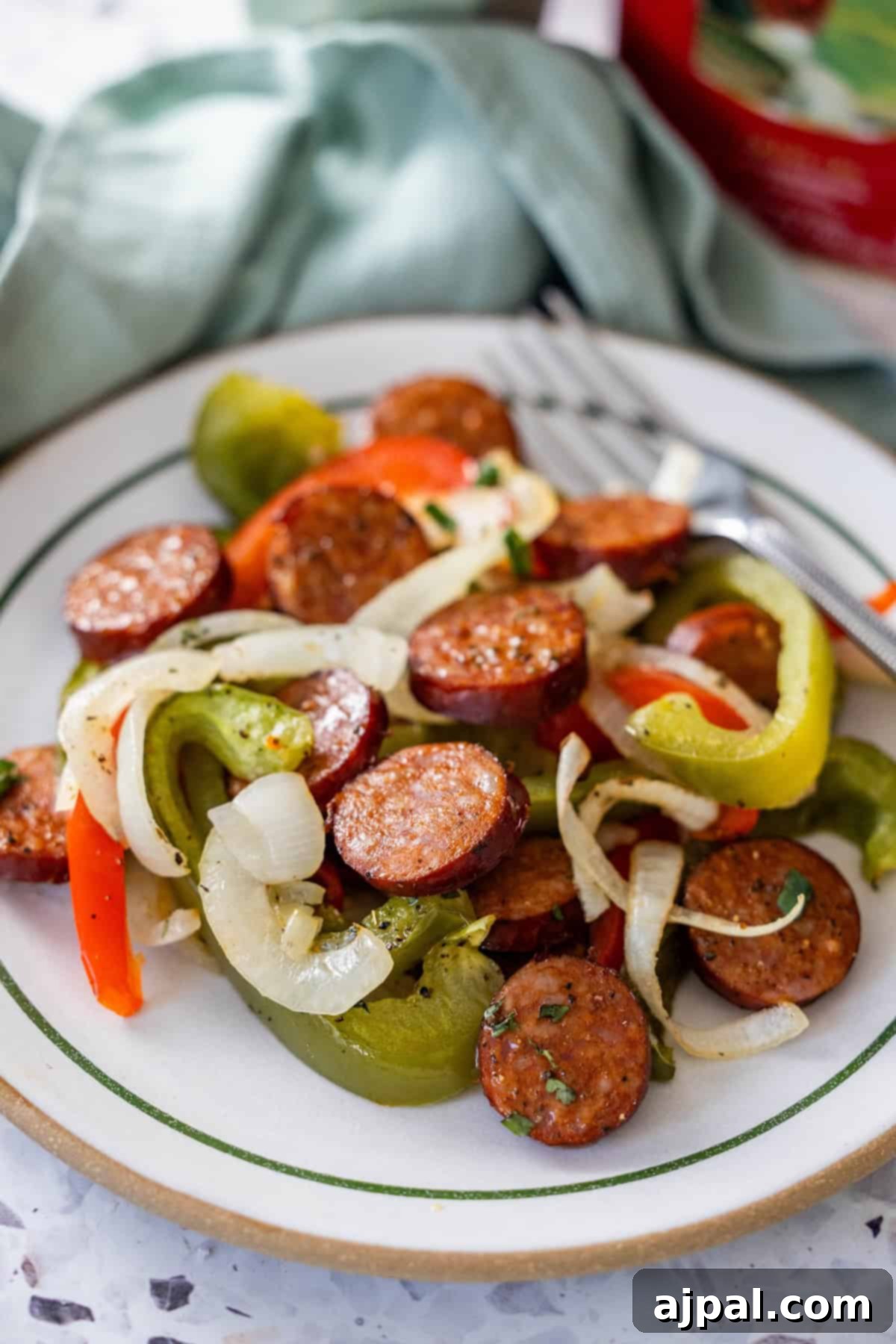 A plate of sliced kielbasa, sautéed onions, and peppers, with a fork placed beside the food.