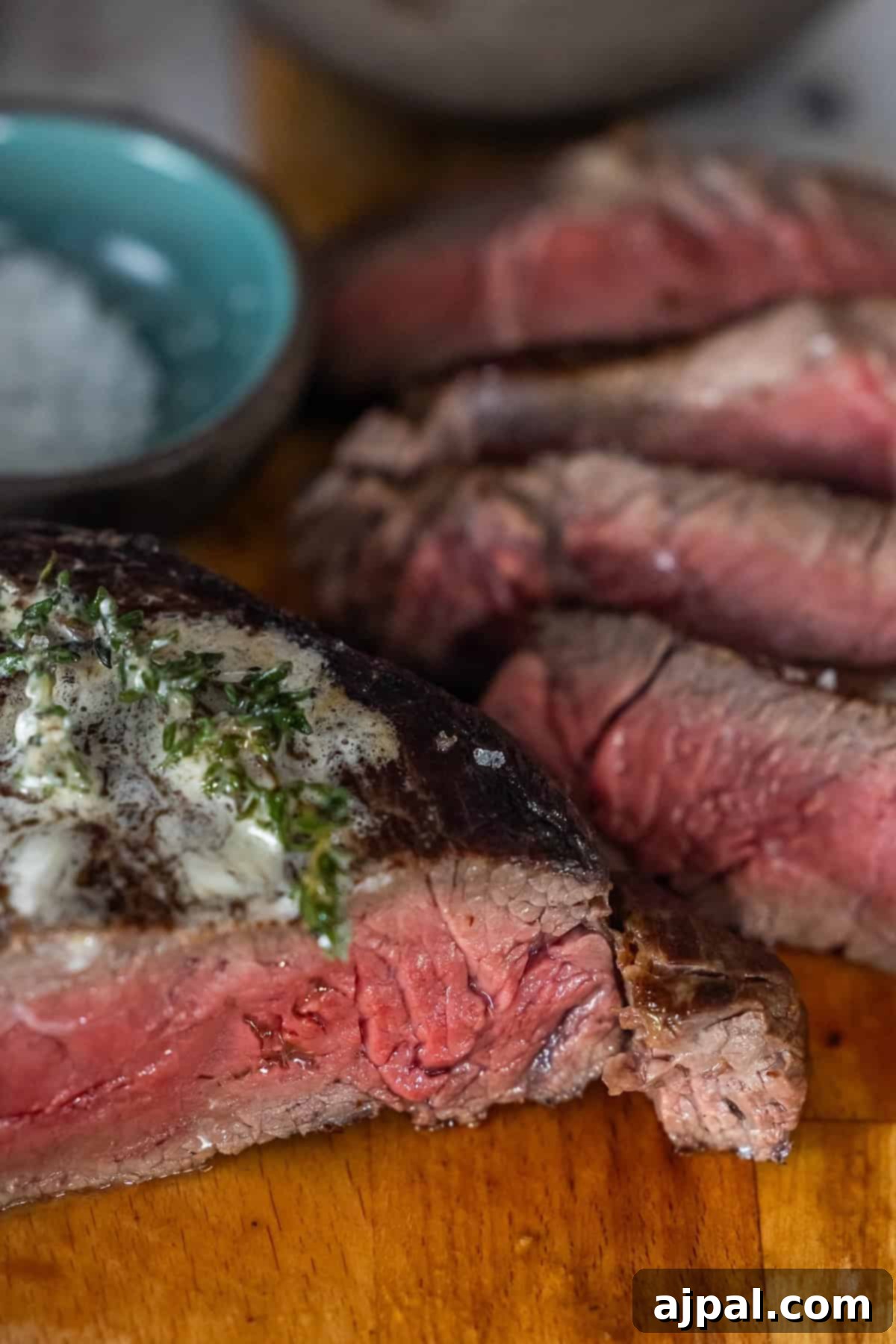 Sliced medium-rare sirloin steak with herb butter and salt.