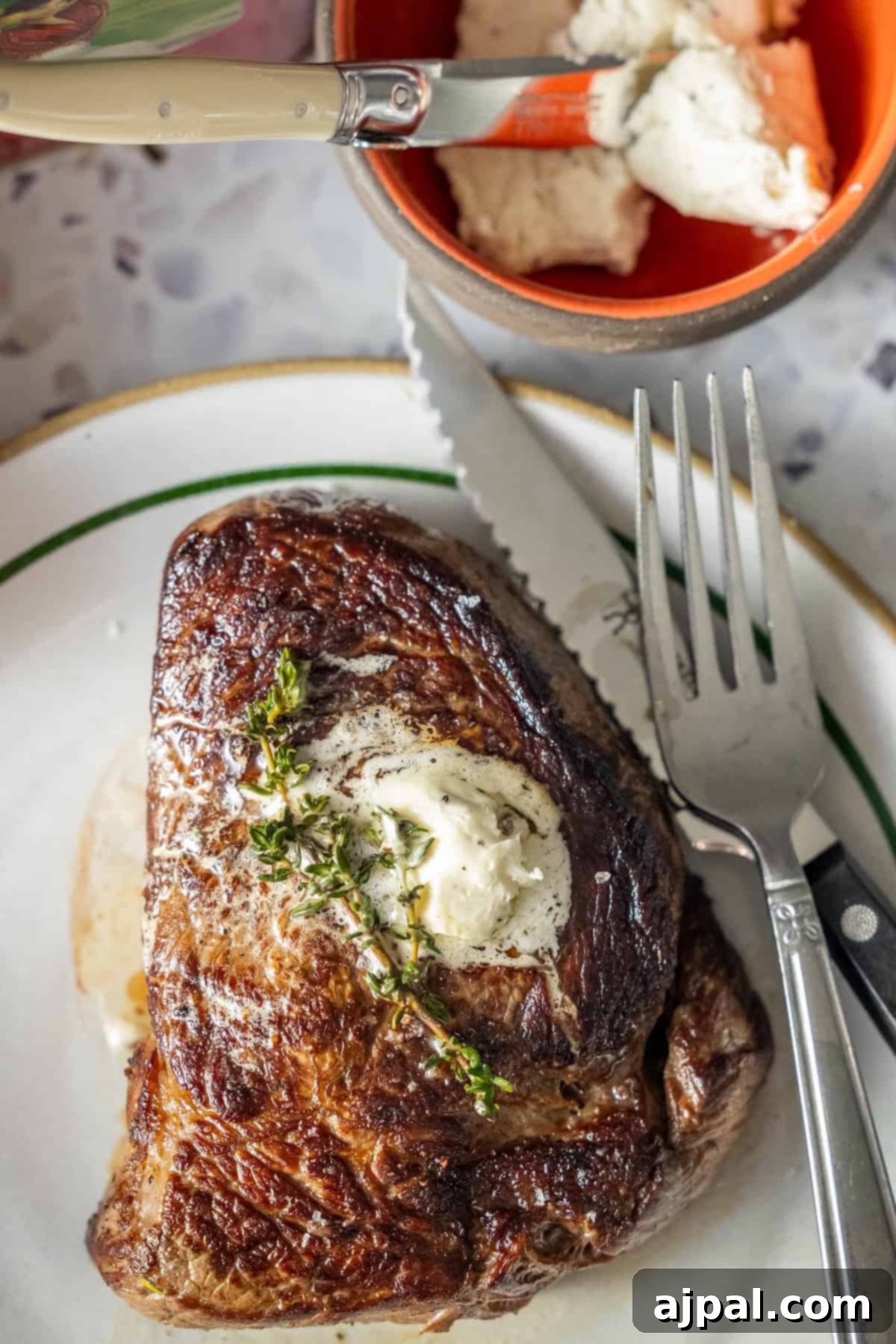 Cooked sirloin steak with herb butter, thyme, and a bowl of butter.