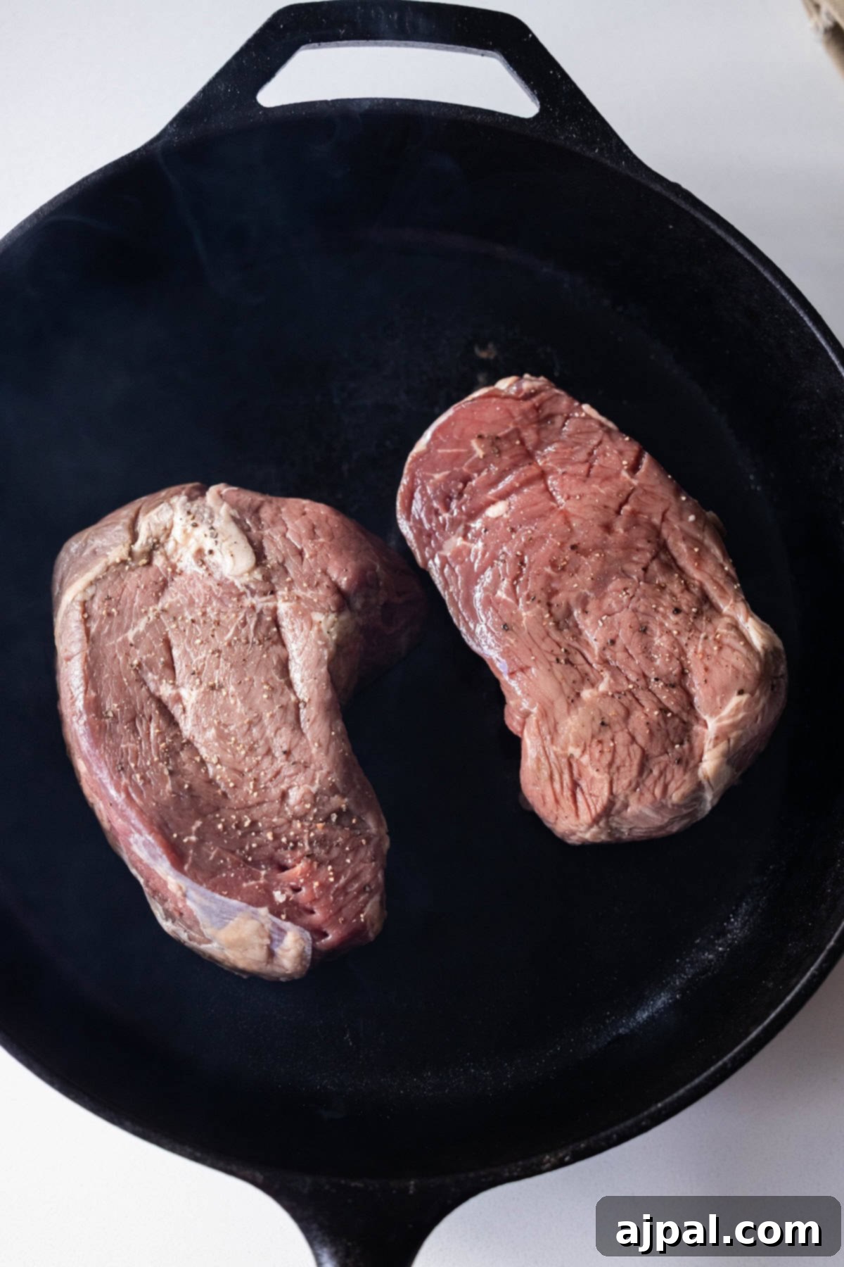 Raw sirloin steaks being cooked in a cast iron skillet.
