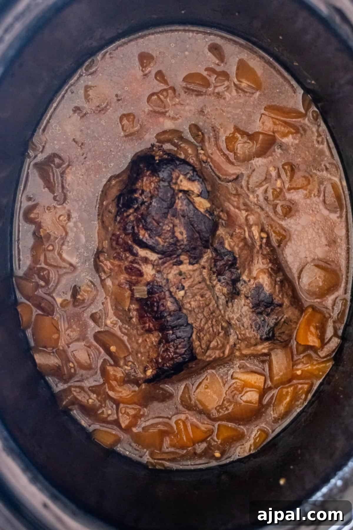 Cooked beef roast in a slow cooker with brown sauce and onions.
