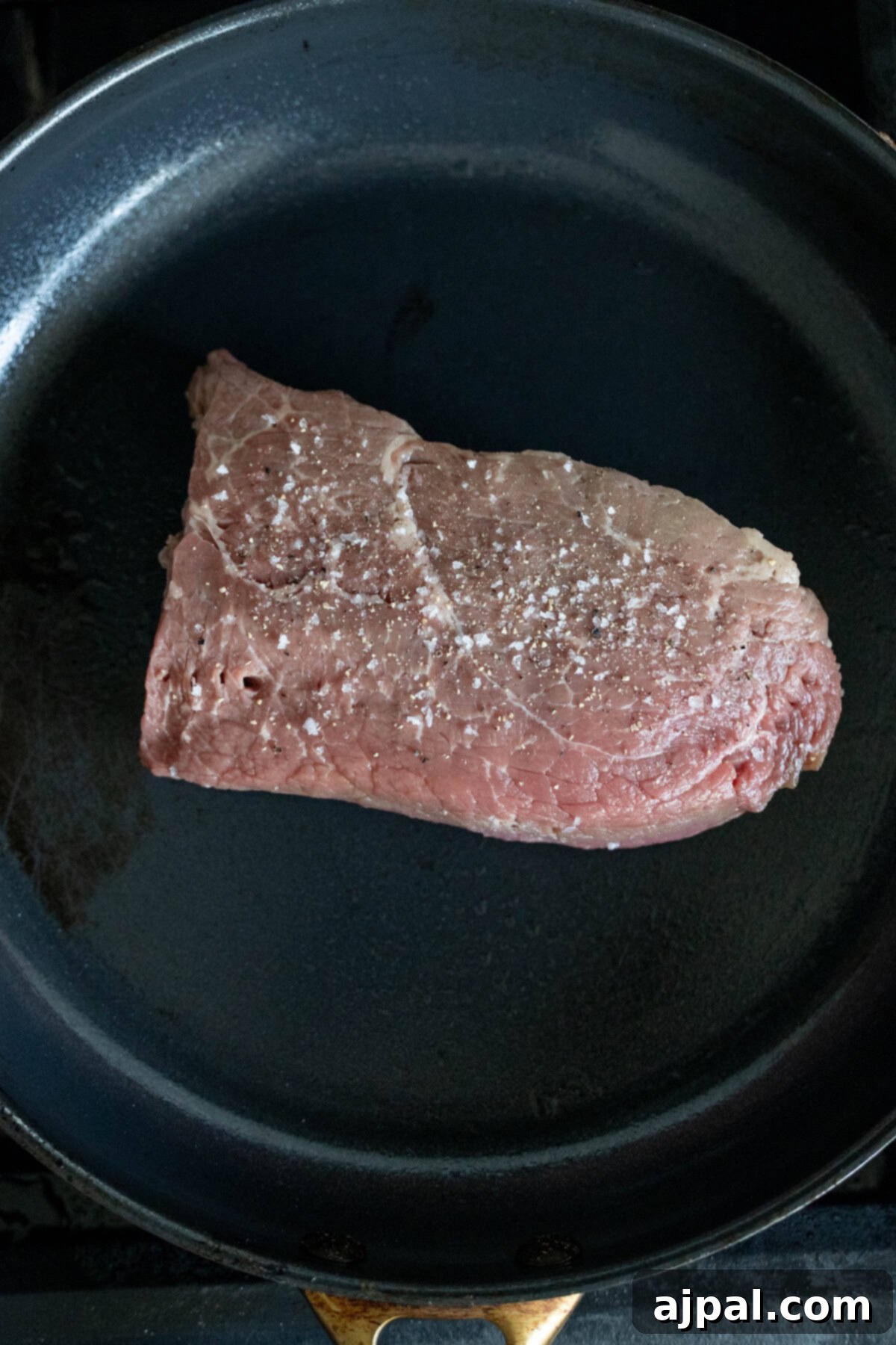 Raw Sirloin Steak seasoned with salt in a frying pan.