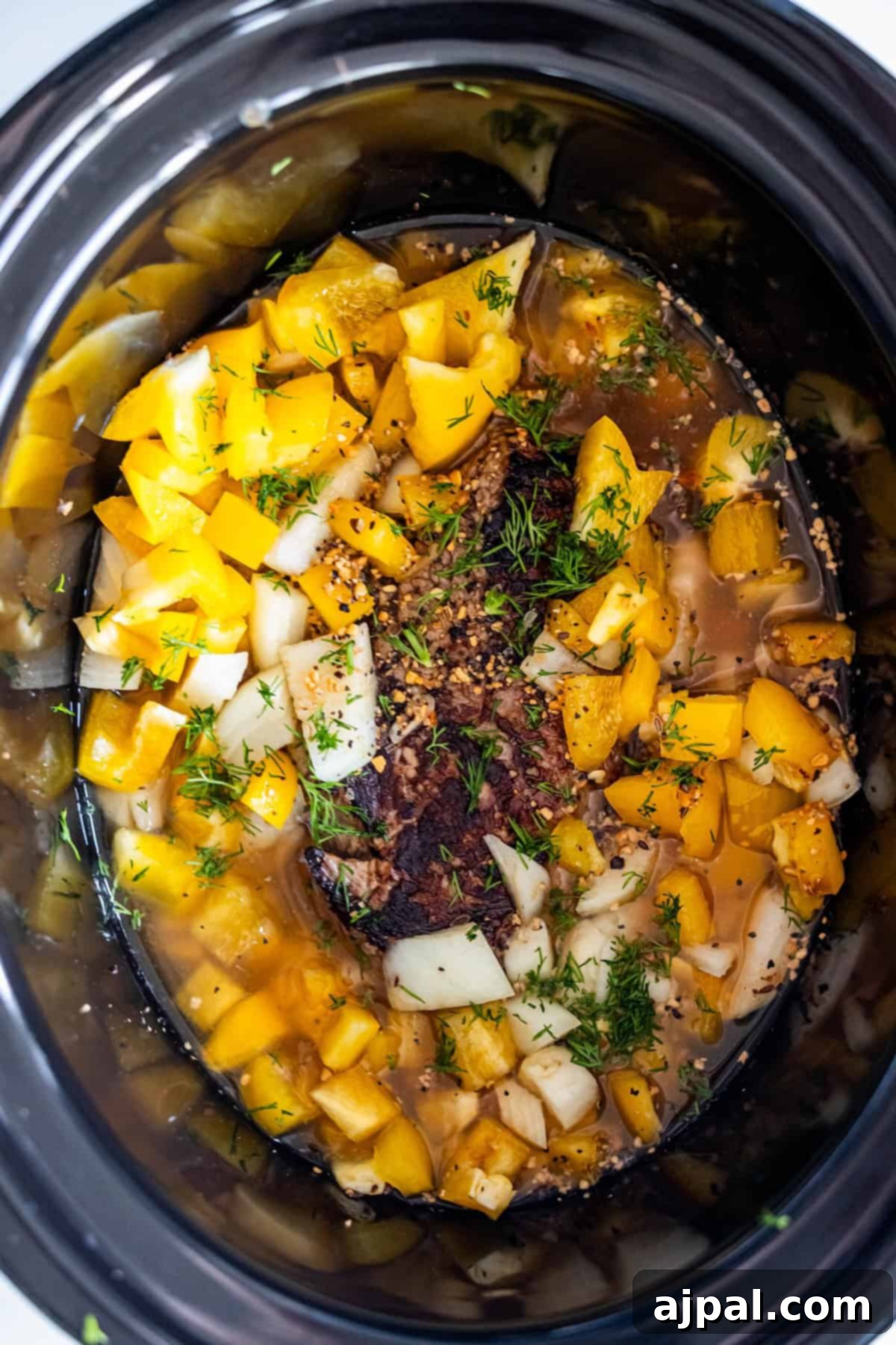 Slow cooker filled with seasoned sirloin steak, peppers, onions and broth.