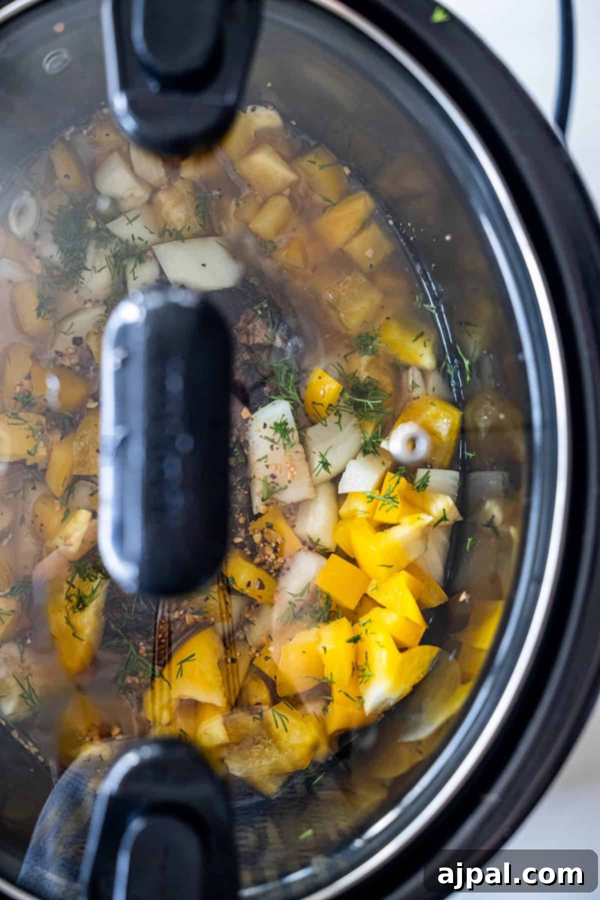 Slow cooker with a glass lid showing vegetables and seasonings simmering.