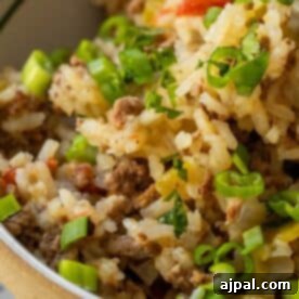 Close-up of a Baked Dirty Rice casserole with ground meat, topped with chopped green onions and herbs.