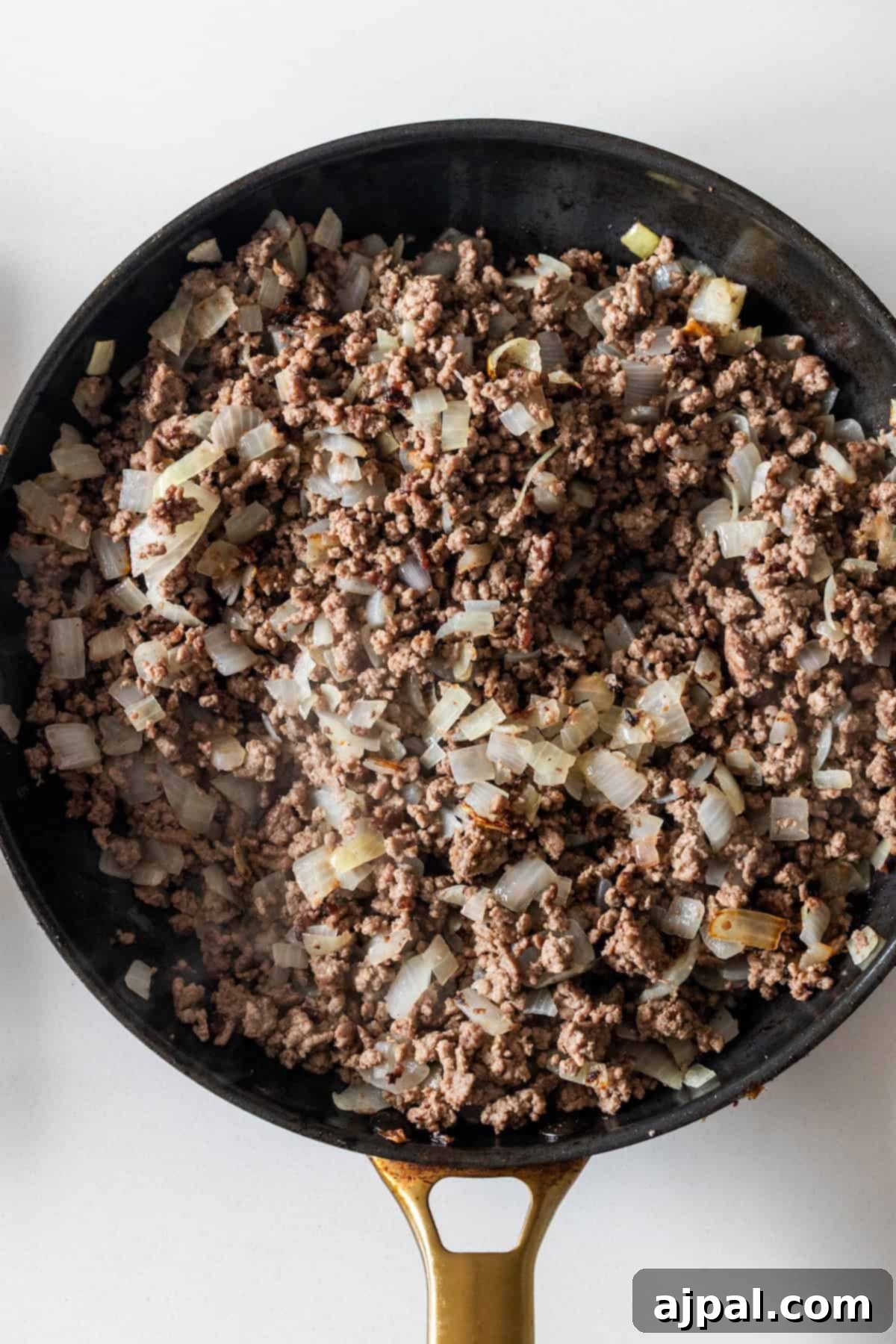 Ground beef and chopped onions cooking in a black skillet with a gold handle—perfect for starting your Dirty Rice Recipe or Baked Dirty Rice.