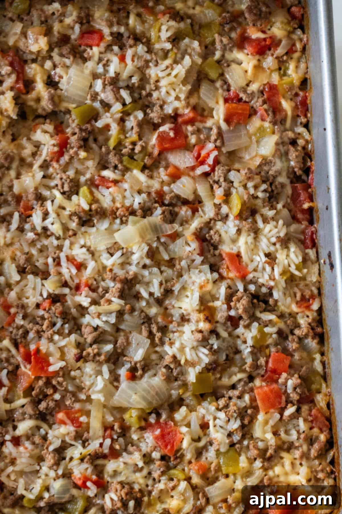 A close-up of a casserole dish filled with baked dirty rice, featuring ground meat, diced tomatoes, onions, and bell peppers.