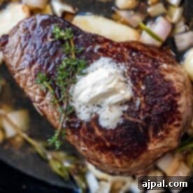 A seared sirloin steak topped with a dollop of butter and a sprig of thyme, surrounded by chopped onions, garlic, and fresh herbs in a pan - the final touches to perfection.