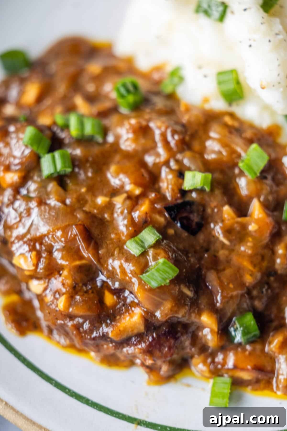 Country Steak in Gravy: A Hearty Homestyle Classic 2 Close-up of country steak in brown gravy with green onions and mashed potatoes.