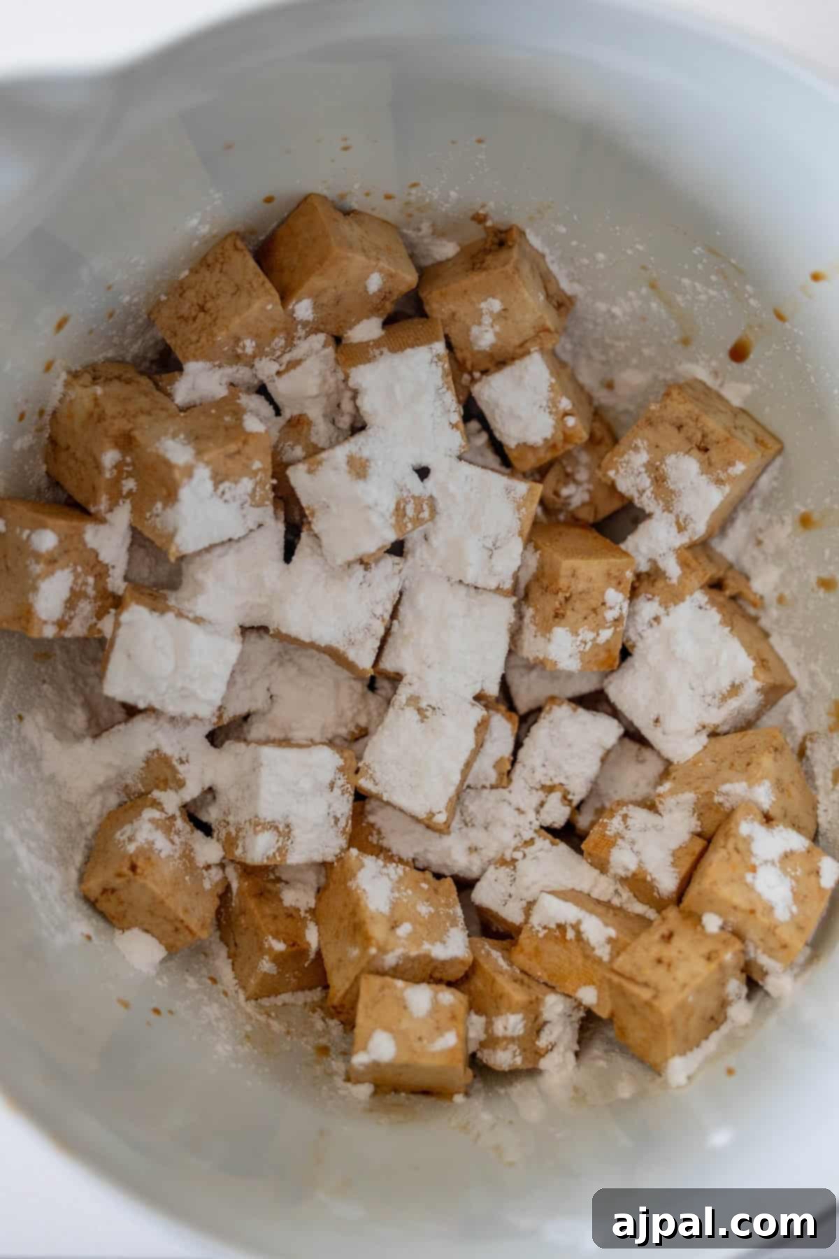 Tofu cubes being tossed in cornstarch.