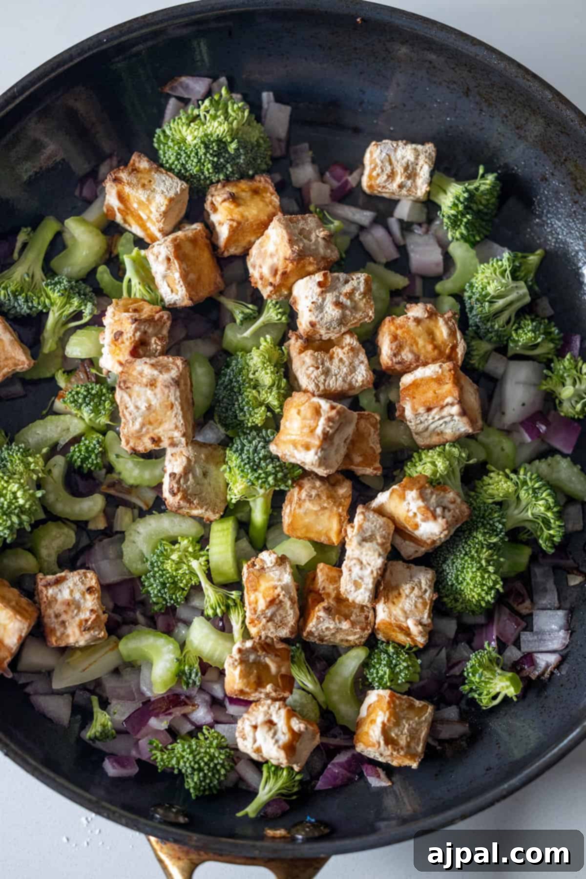 Broccoli, celery, and onions cooking in a skillet.