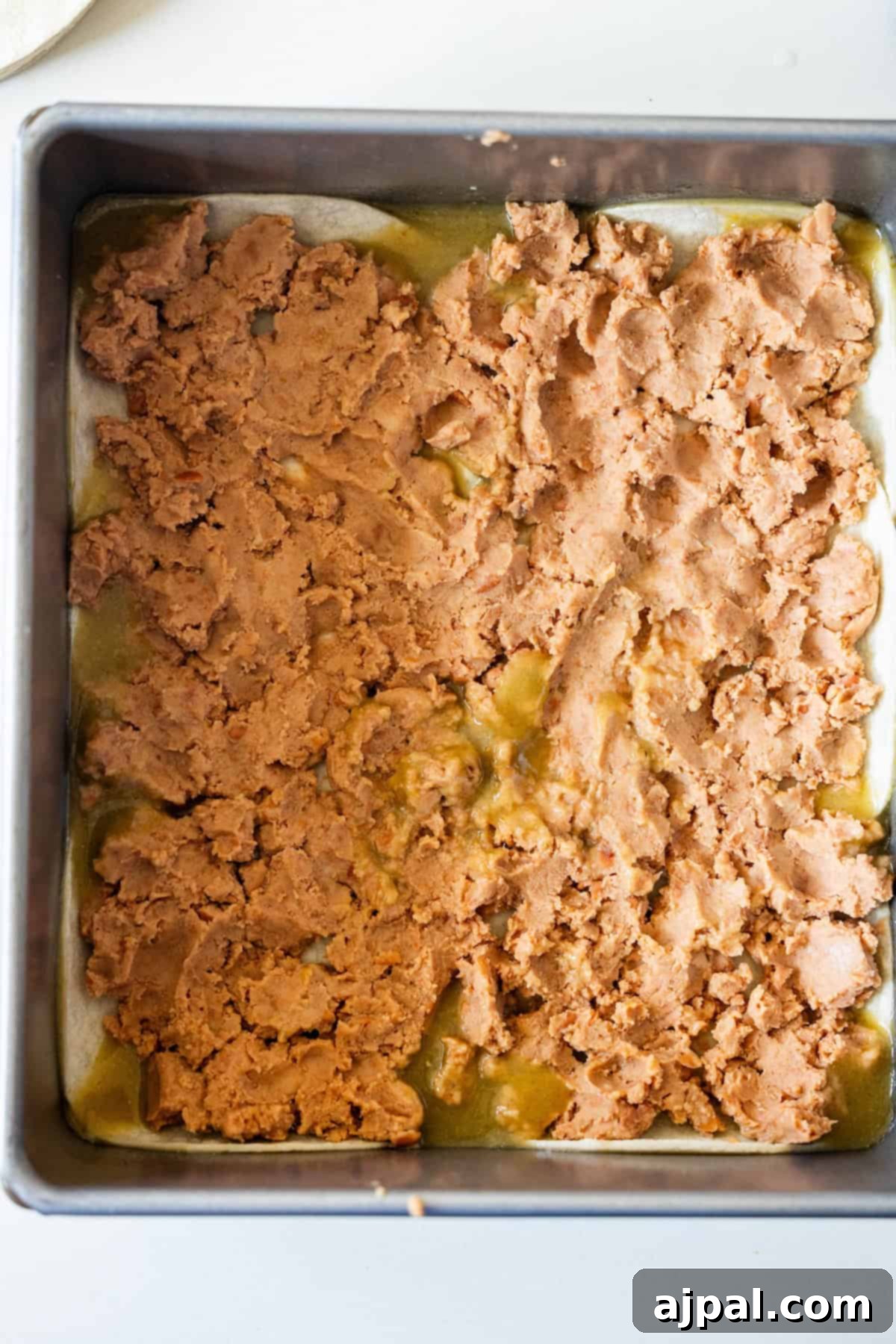 Layer of tortillas and refried beans in a baking pan