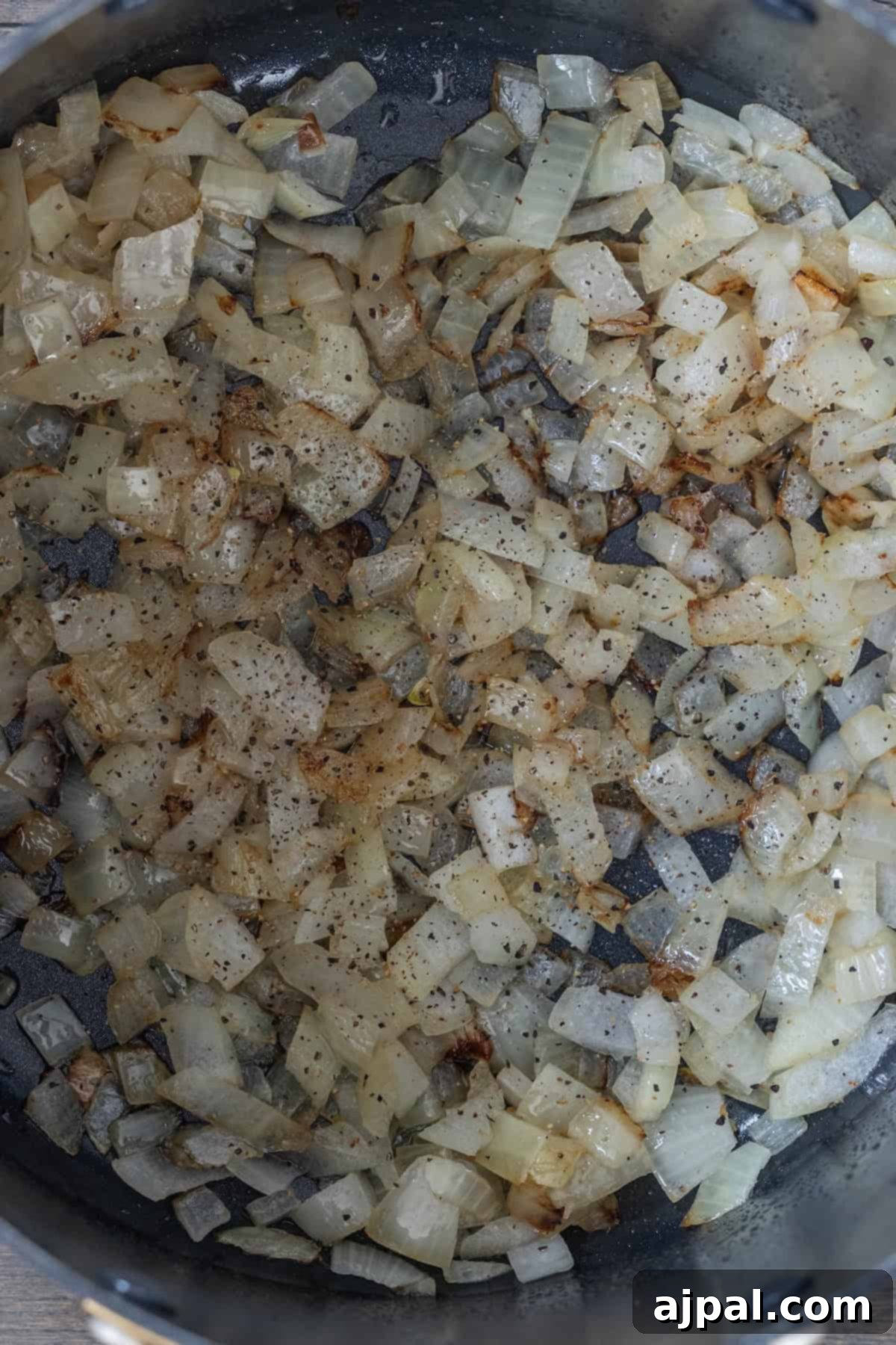 Chopped onions sautéing in a pan with bacon, lightly browned and sprinkled with visible seasoning.