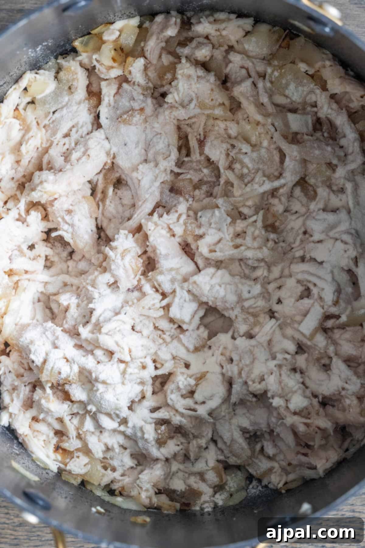 Shredded cooked chicken mixed with sautéed onions, sprinkled with flour in a pot—perfect as a base for savory Cheesy Corn Chowder.