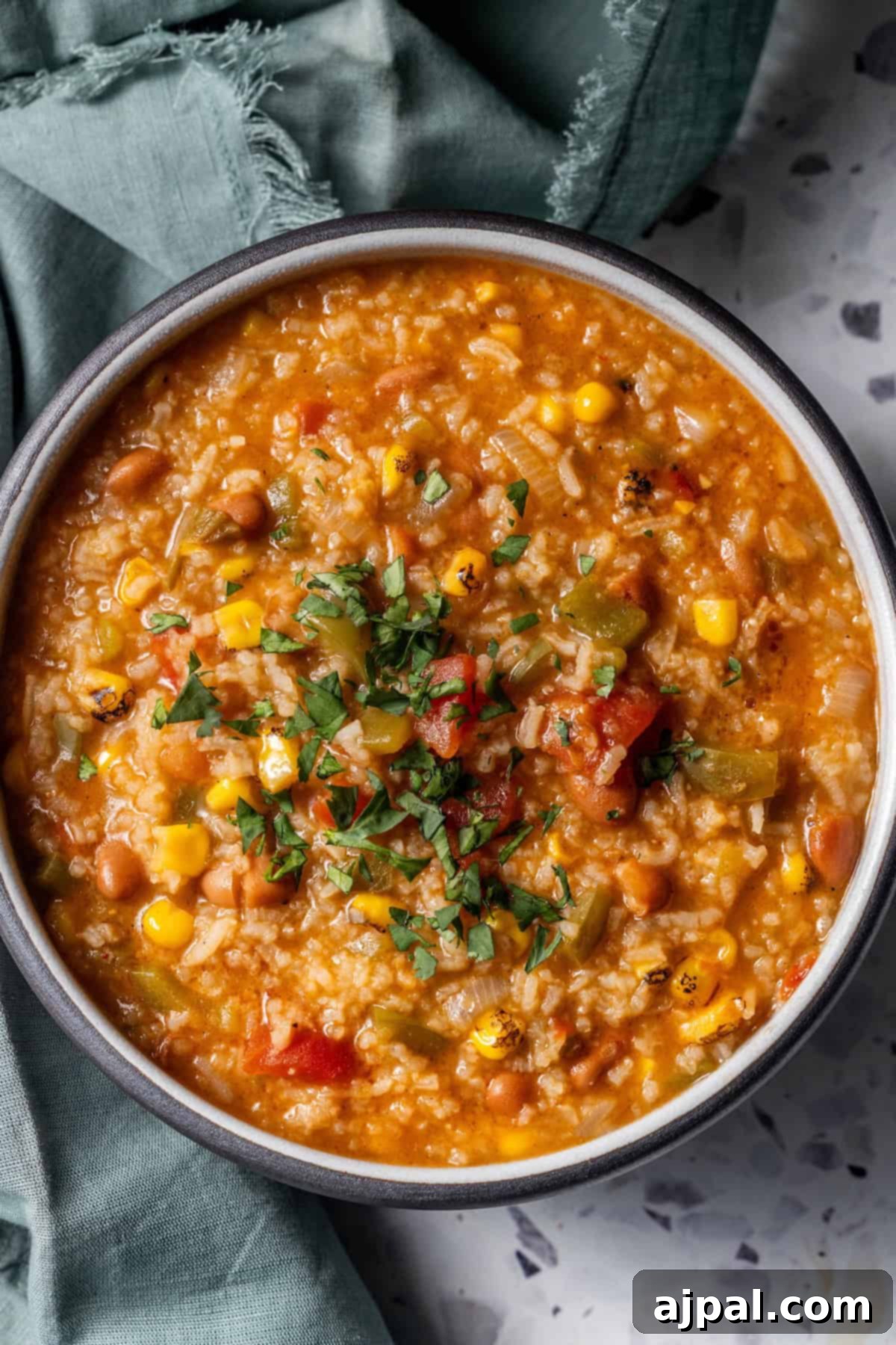 A bowl of flavorful vegan vegetable and rice soup with corn, beans, tomatoes, and fresh herbs.