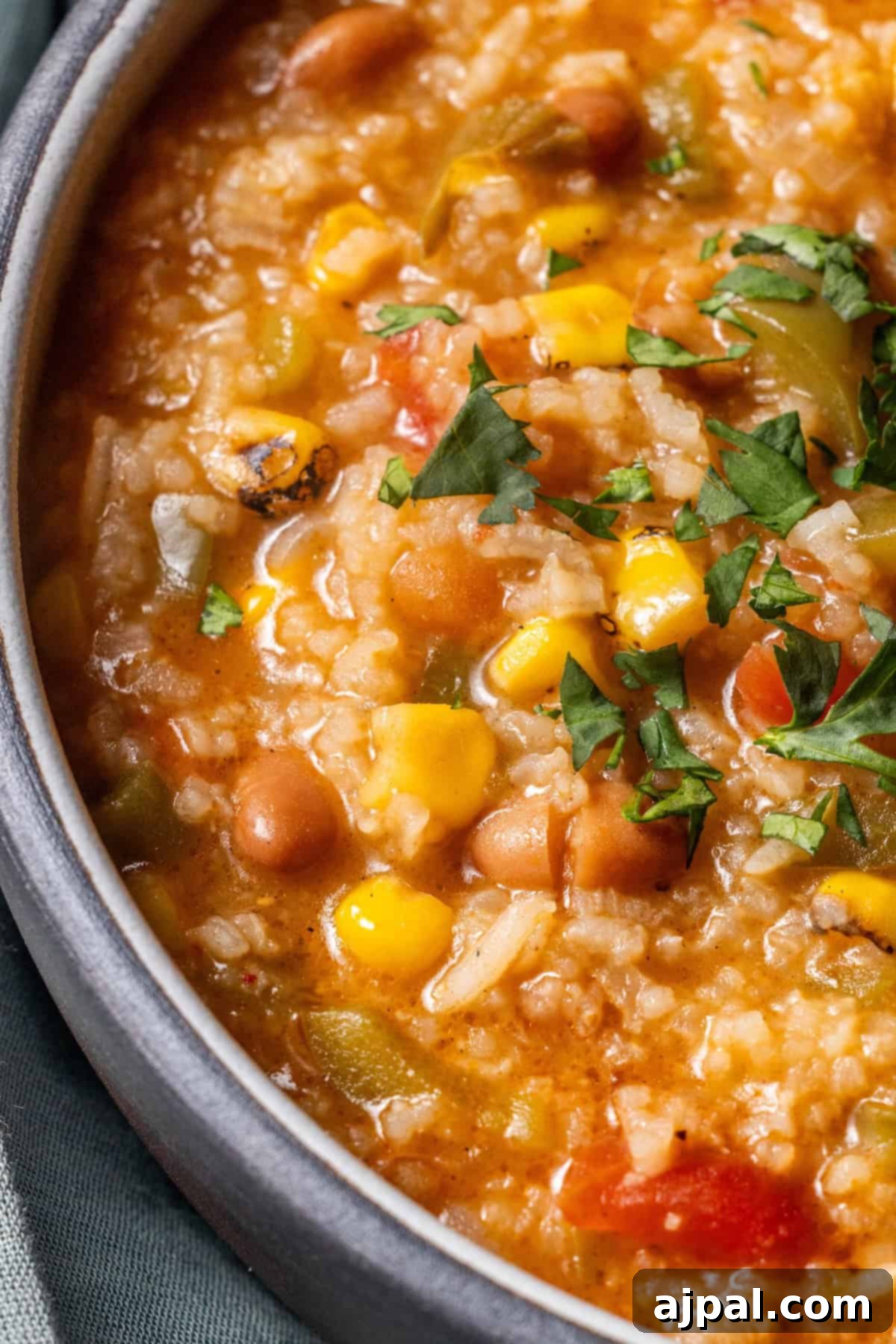 A close-up of vegan vegetable and bean soup with corn, tomatoes, rice, and chopped cilantro garnish.